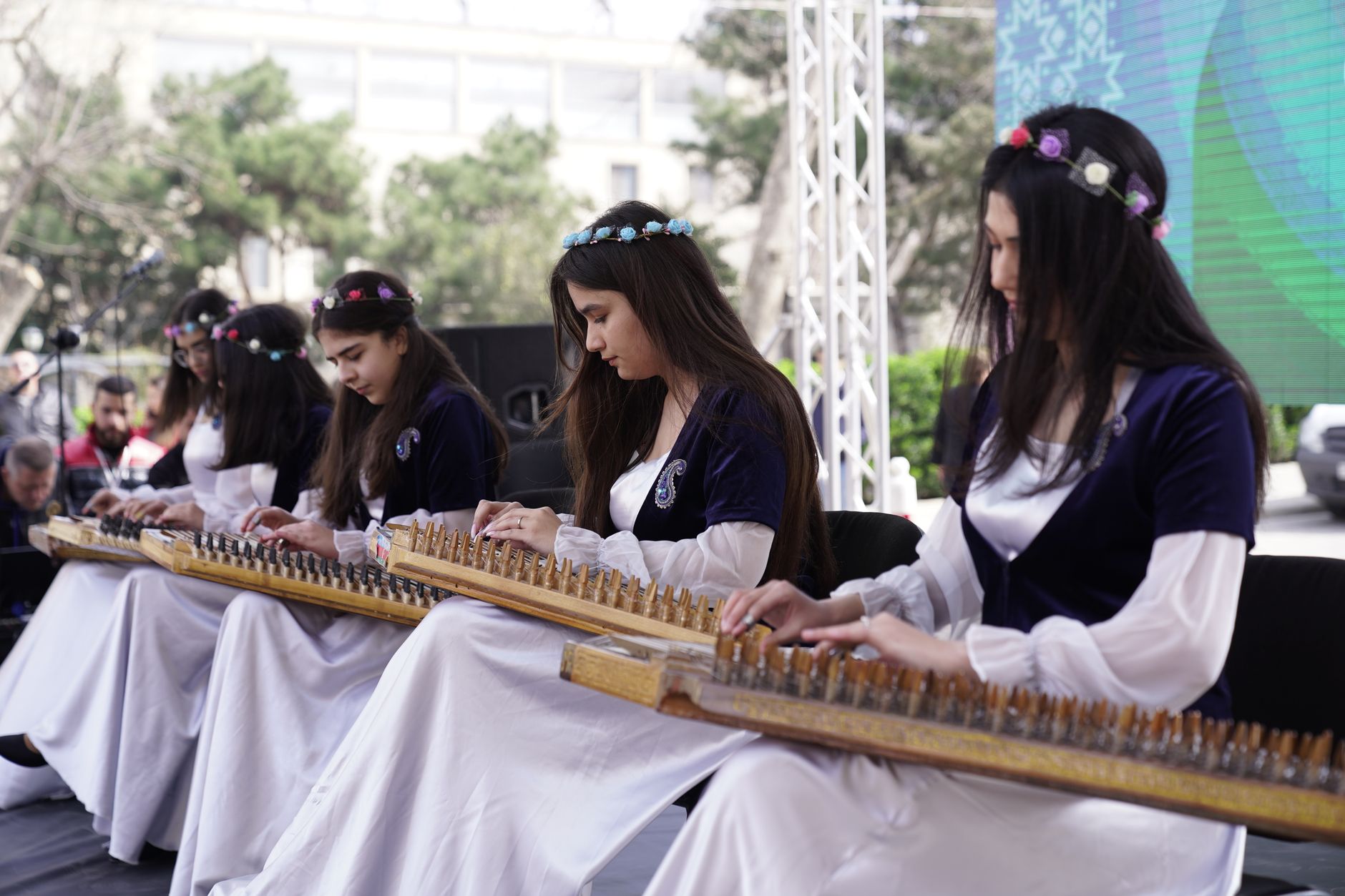 Group of women playing traditional string instruments outdoors, wearing floral headbands.
