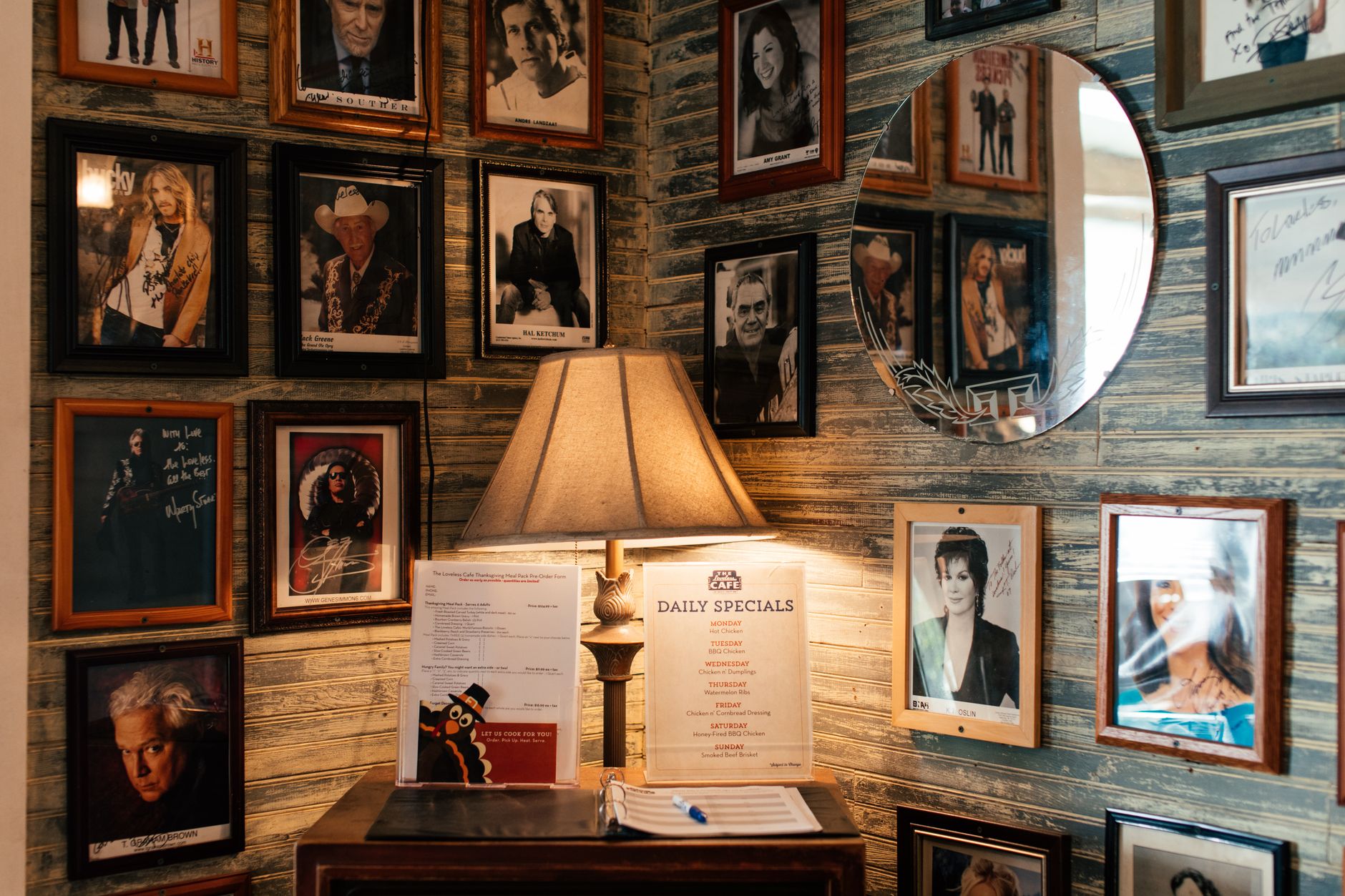 Warm room features celebrity photos on a vintage wall with a cozy lamp illuminating a menu.