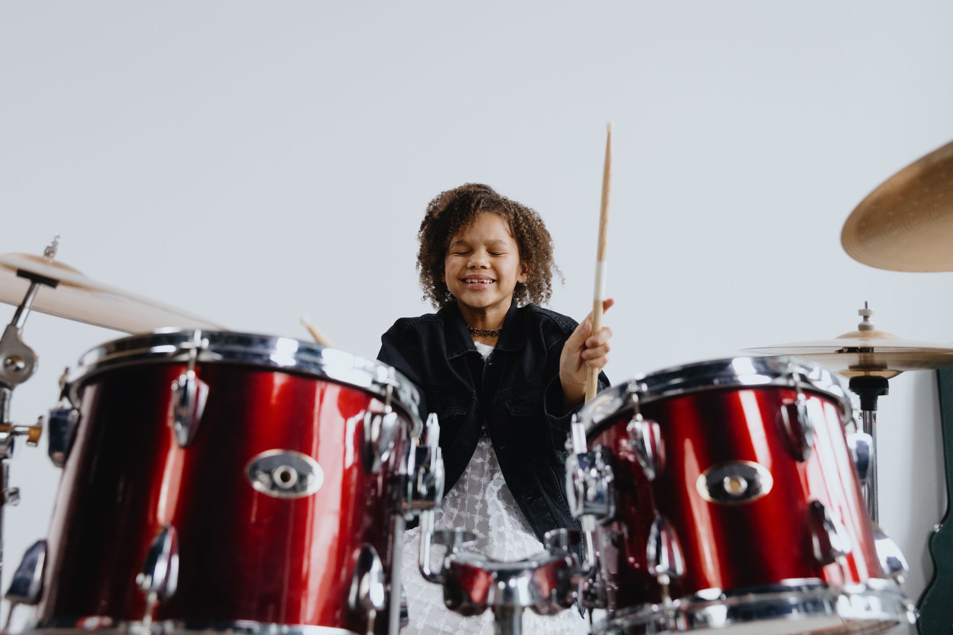 Happy young girl playing drums indoors, enjoying music with a joyful smile.