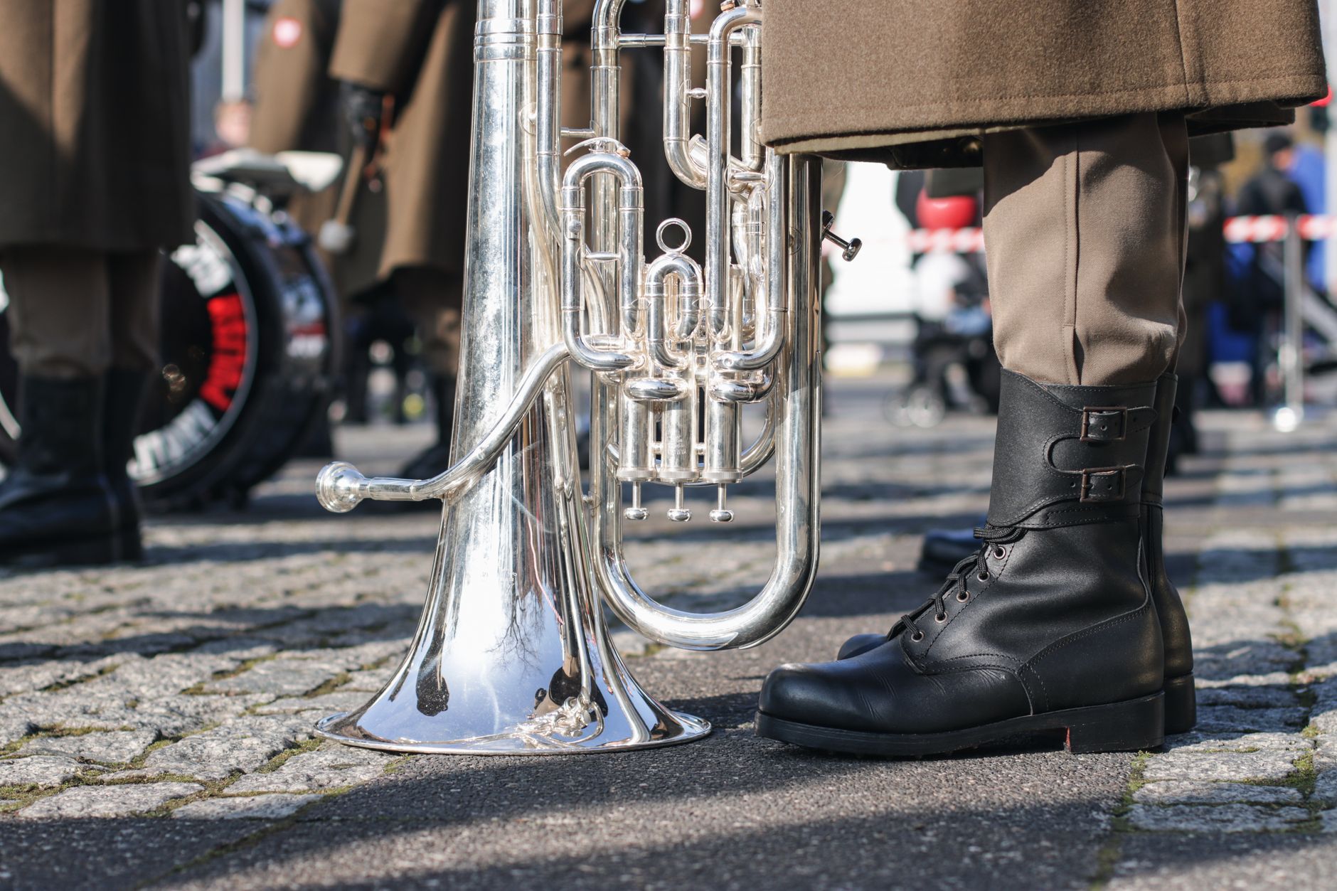 Close-up of military band boots and brass instrument on a cobblestone street during a parade.