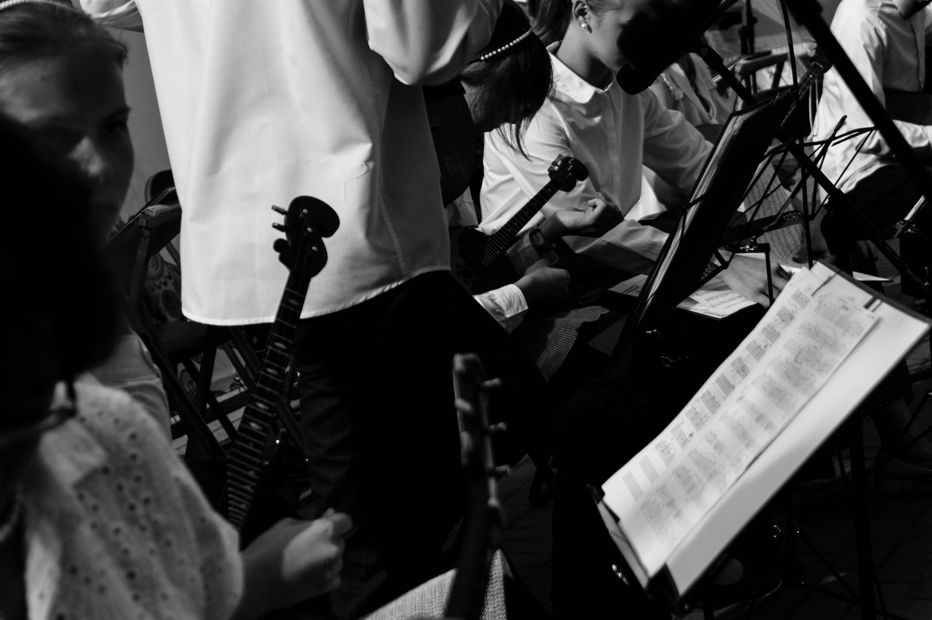 Monochrome shot of musicians rehearsing with string instruments and sheet music.