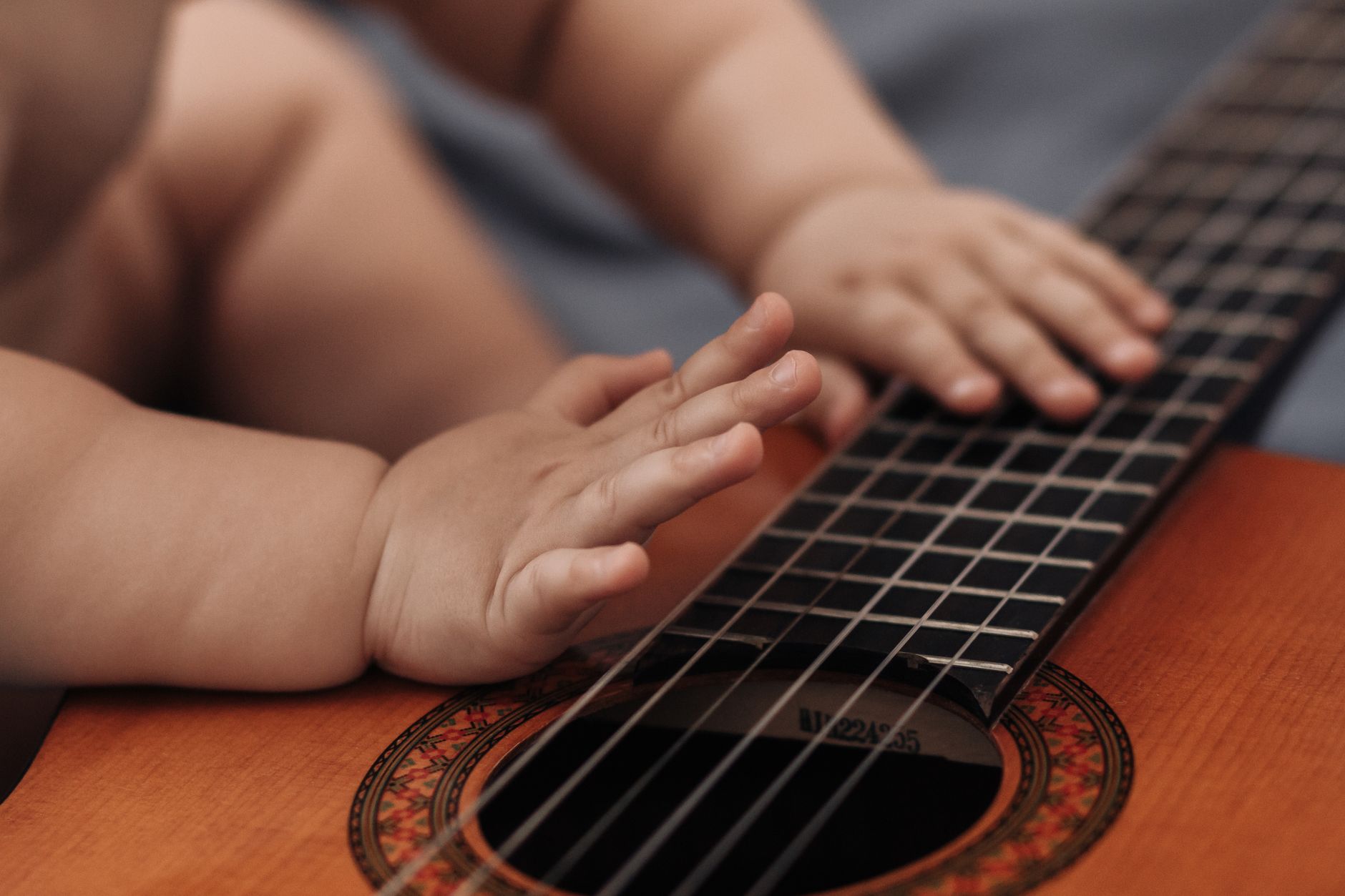 Adorable baby hands gently touching acoustic guitar strings, creating a musical moment.