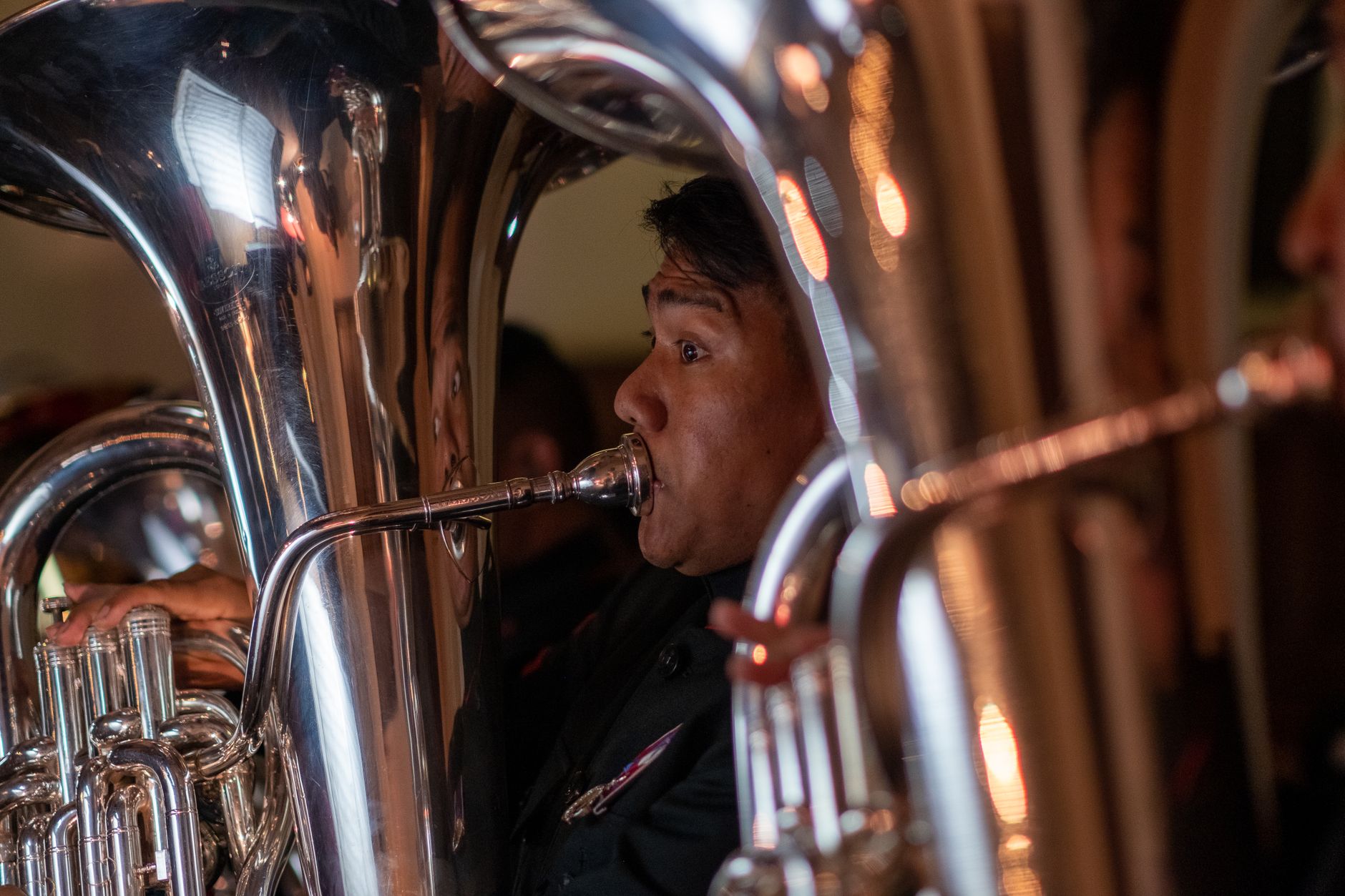 Close-up of a musician playing a tuba at an indoor concert, highlighting the shiny brass instrument.