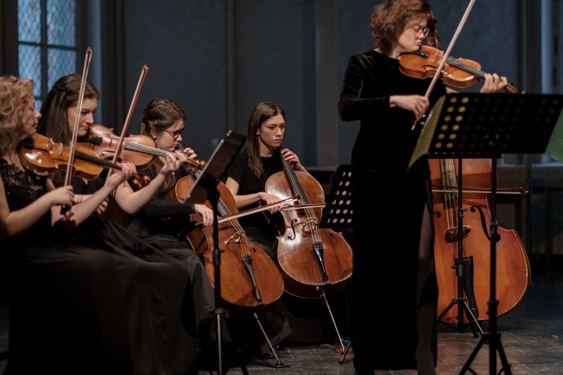 A group of women musicians performing classical music with violins and cellos in an orchestral setting.