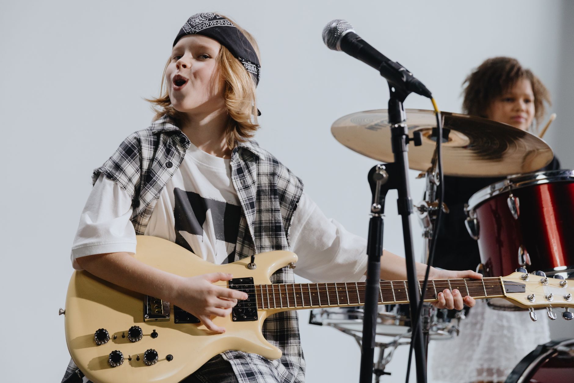 Young musicians passionately playing electric guitar and drums on stage, showcasing kids' musical talent.