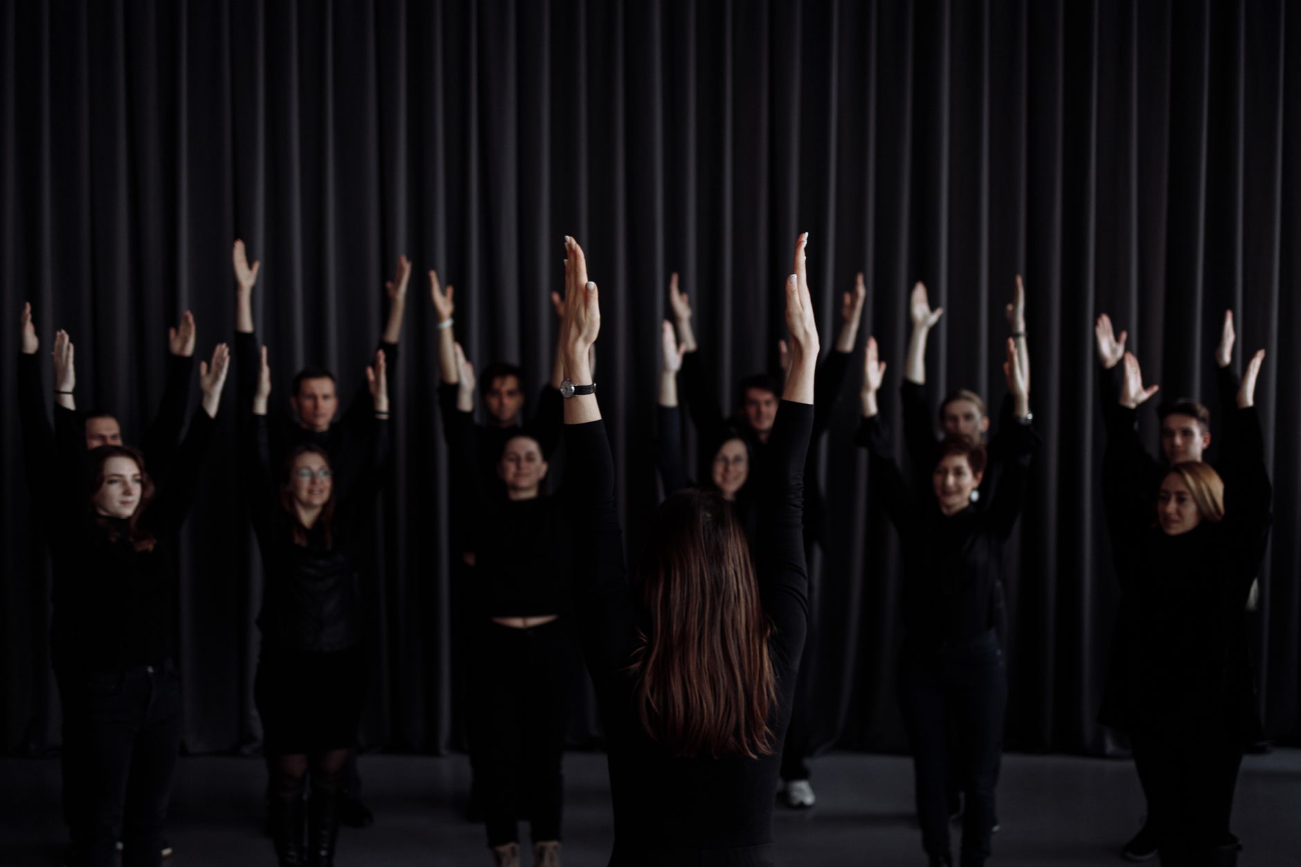 A group of performers rehearsing a contemporary dance with raised arms indoors.