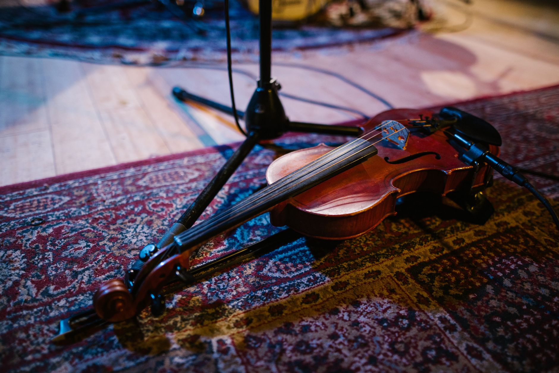 A violin placed on a patterned rug next to a mic stand, evoking musical ambiance.