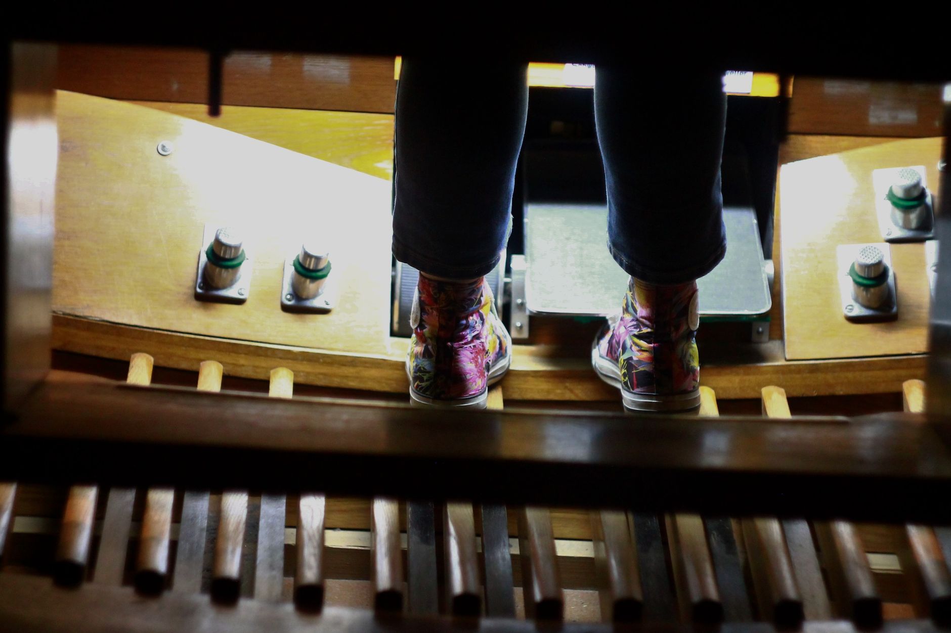 A child in colorful shoes operating the foot pedals of an organ. Close-up shot with focus on the sneakers.