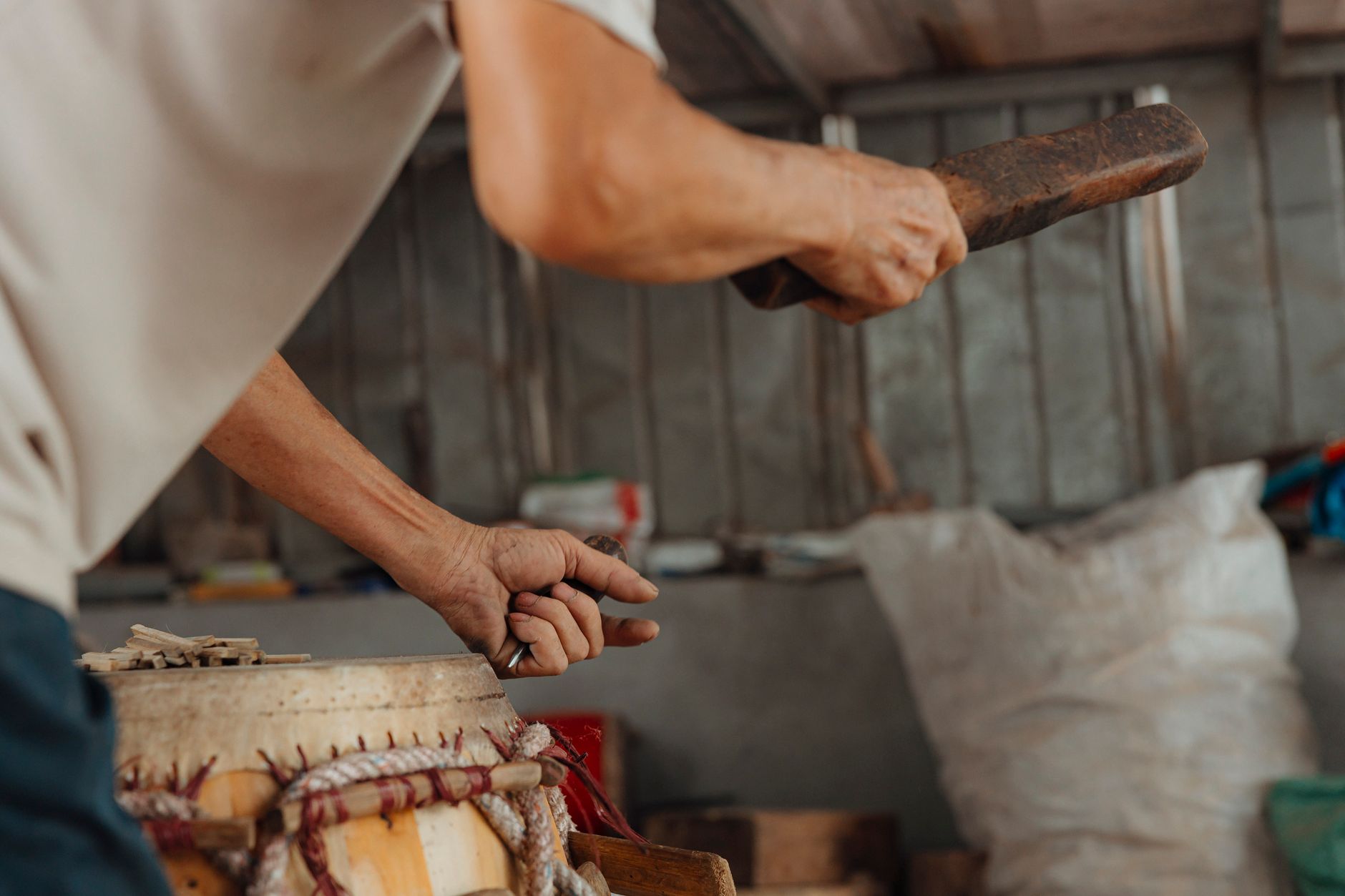 A close-up of a craftsman shaping a traditional drum with a tool indoors.