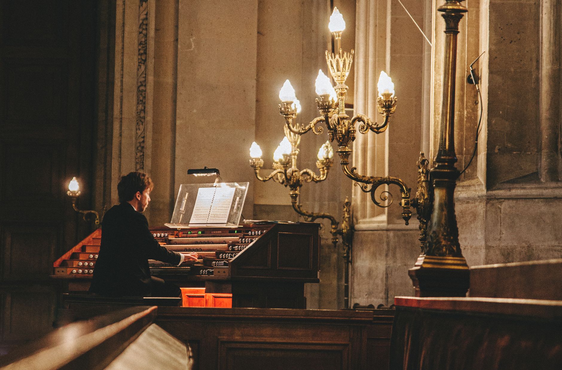 Elegant scene of an organist playing in a historic Paris church, illuminated by ornate chandeliers.