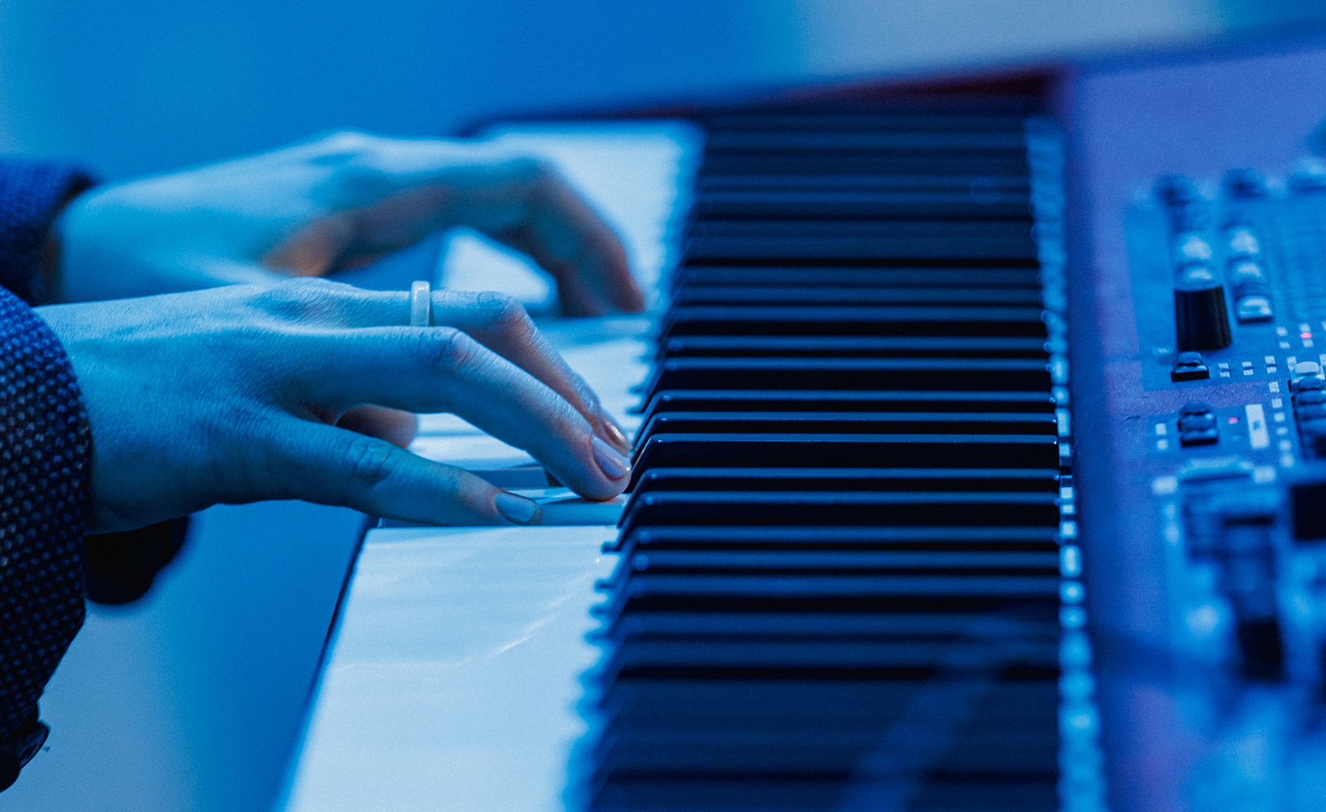 Hands playing electronic keyboard with a cool blue tone.
