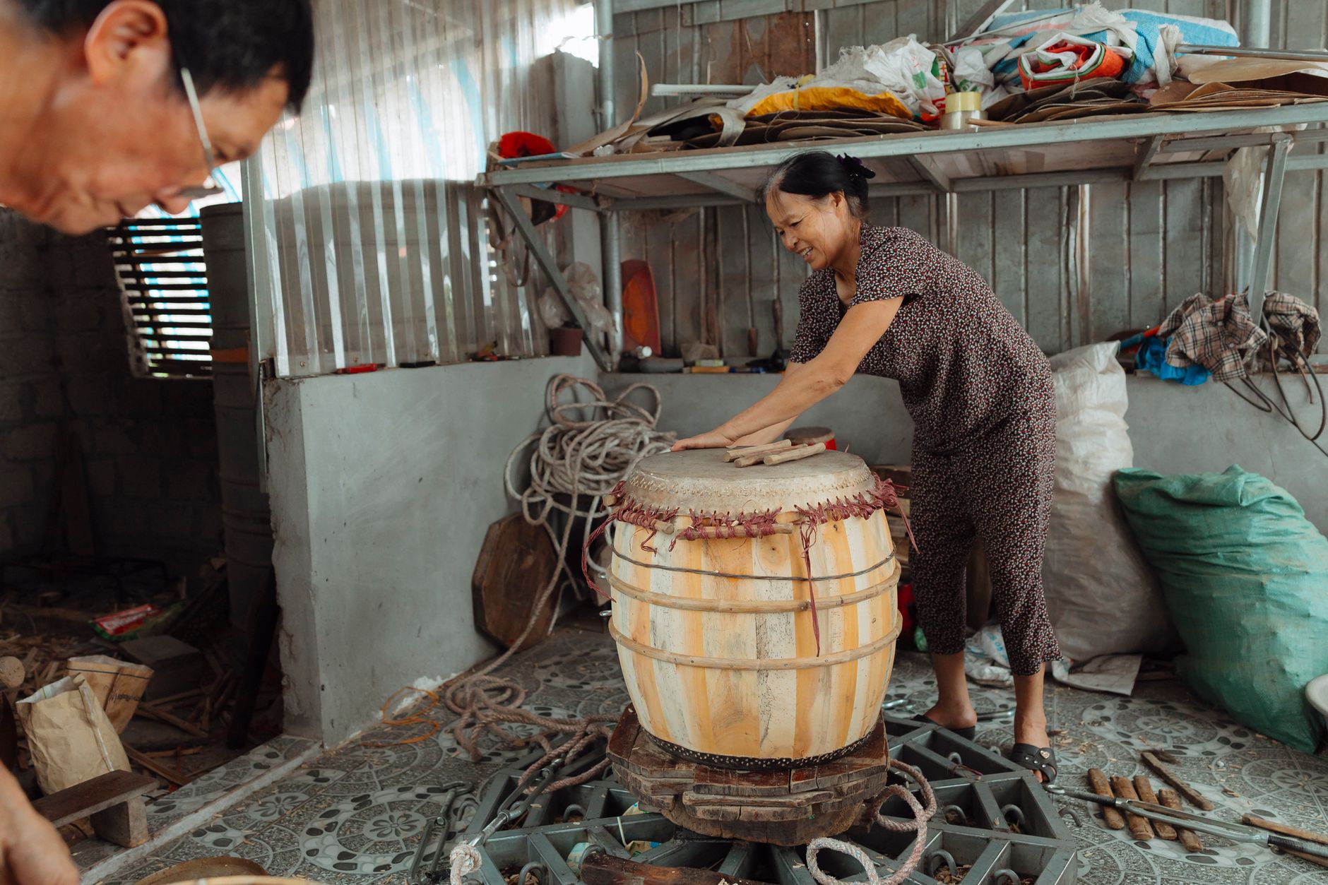 A woman skillfully making a wooden drum in a rustic indoor workshop setting.