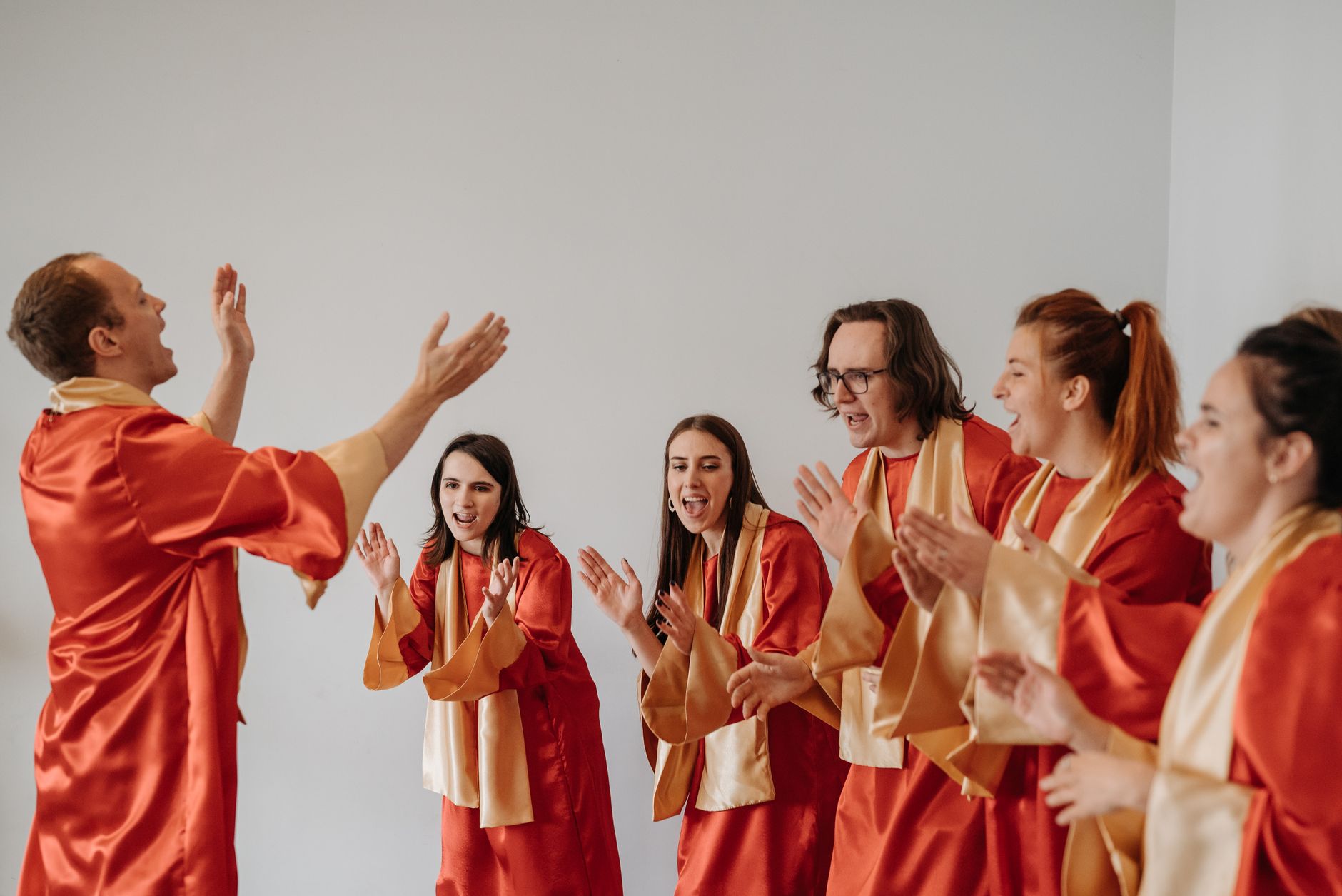 A group of adult choir singers in red robes clapping and singing indoors.