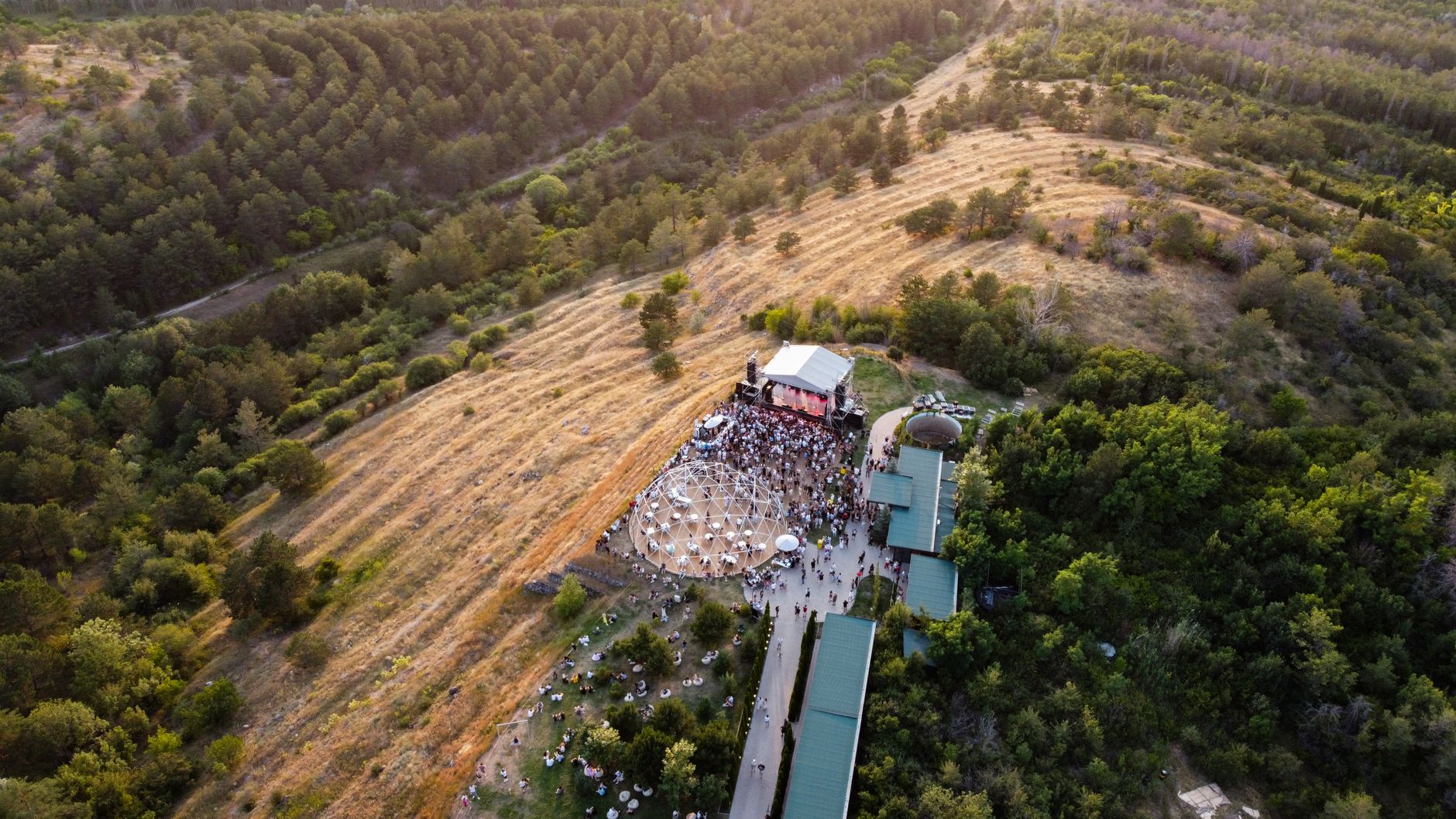 A scenic aerial shot capturing a lively outdoor music festival surrounded by lush greenery in Kotayk Province, Armenia.