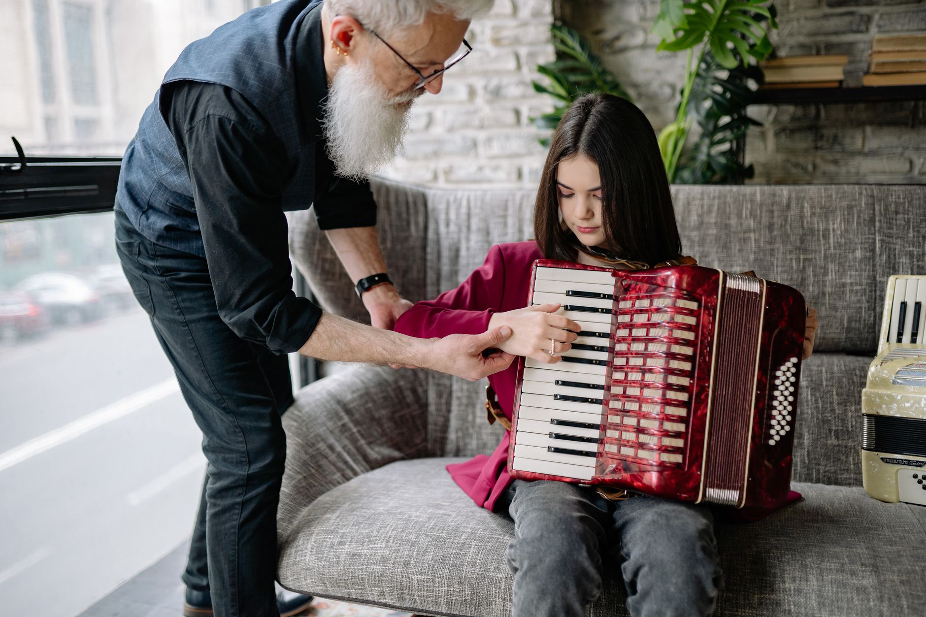 Elderly man teaching young girl to play accordion indoors, fostering musical skills.