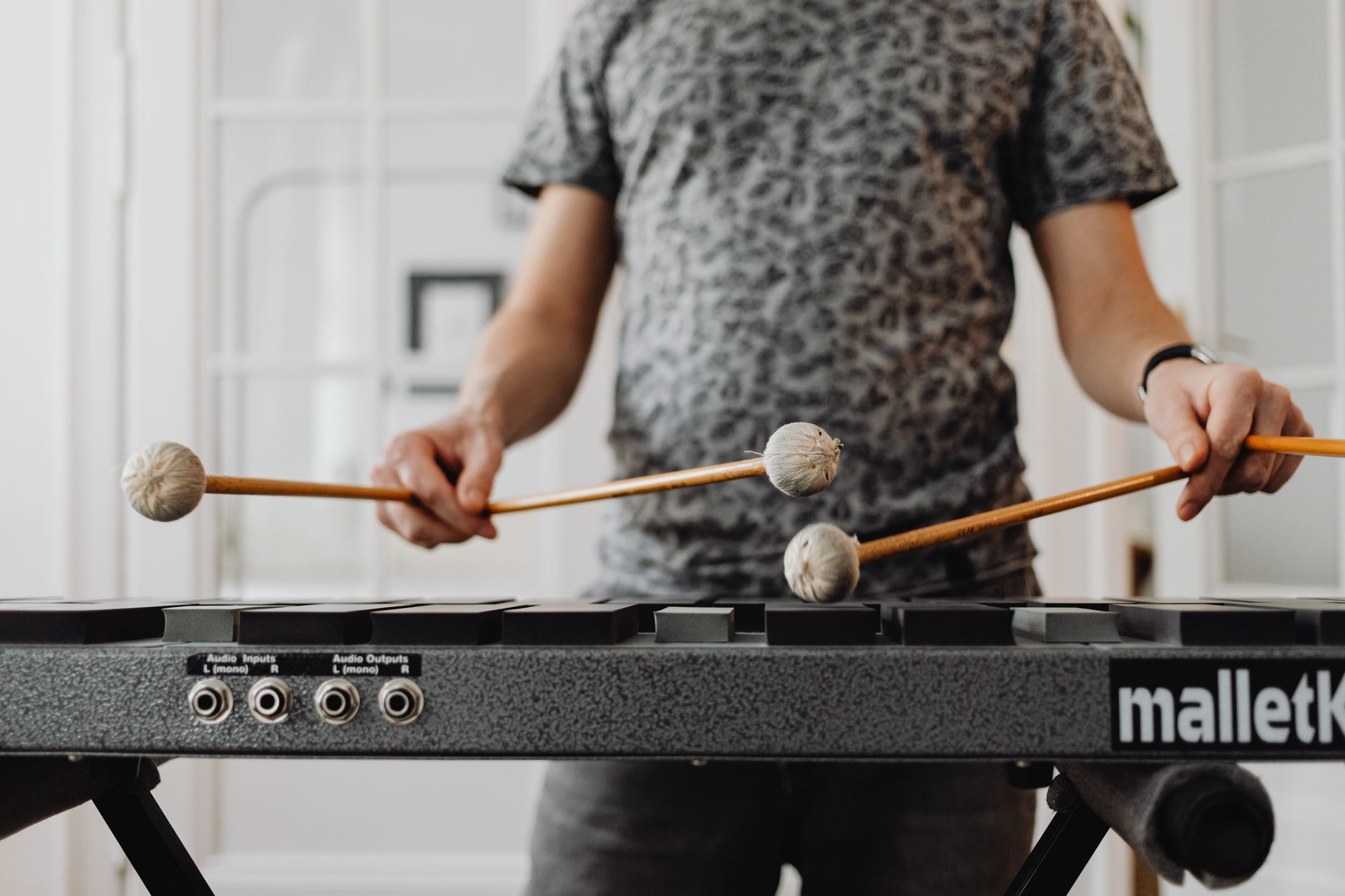 Adult musician practicing on a xylophone with mallets indoors, focusing on rhythm and technique.