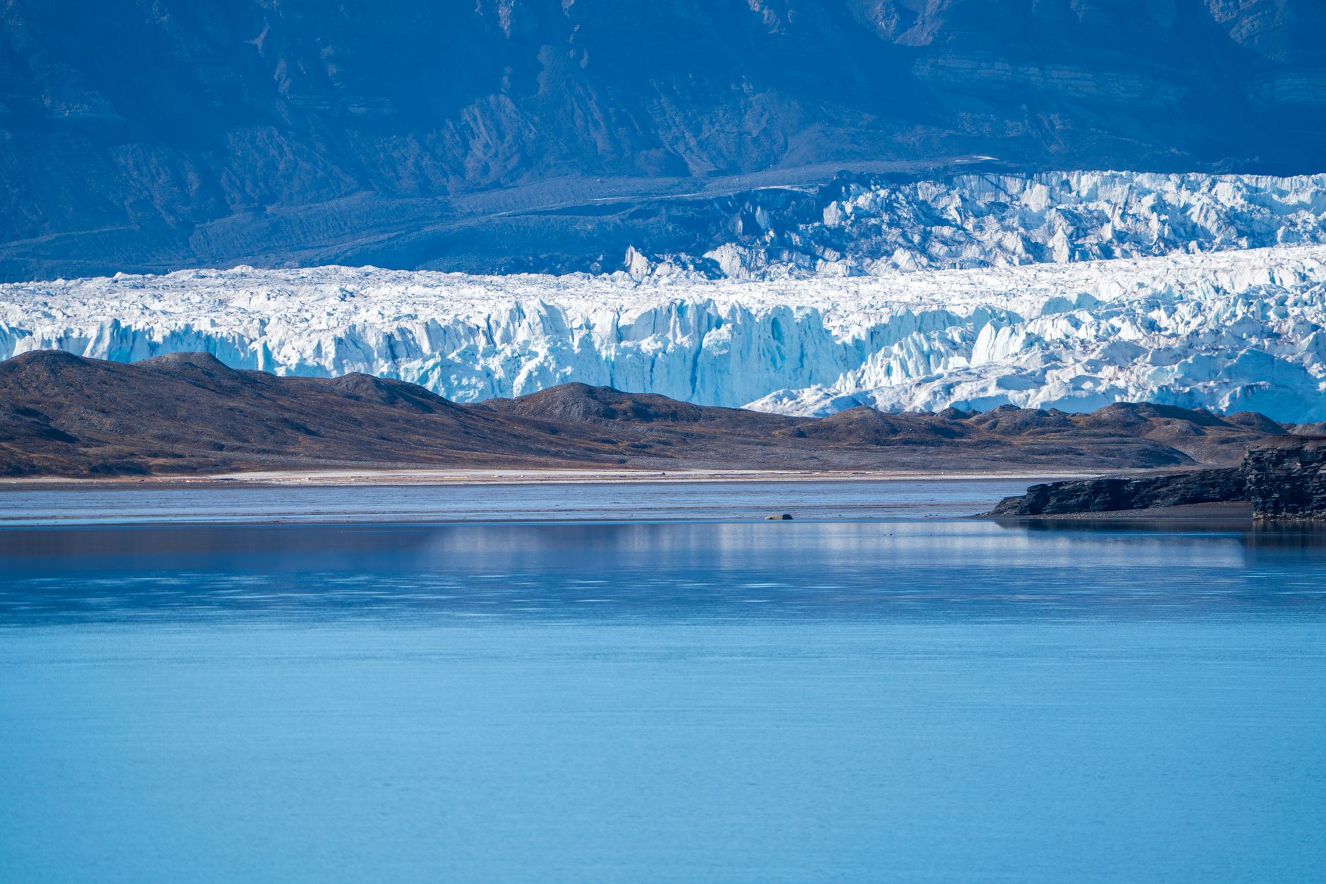Scenic view of a glacier with icy cliffs meeting a tranquil fjord in Svalbard.