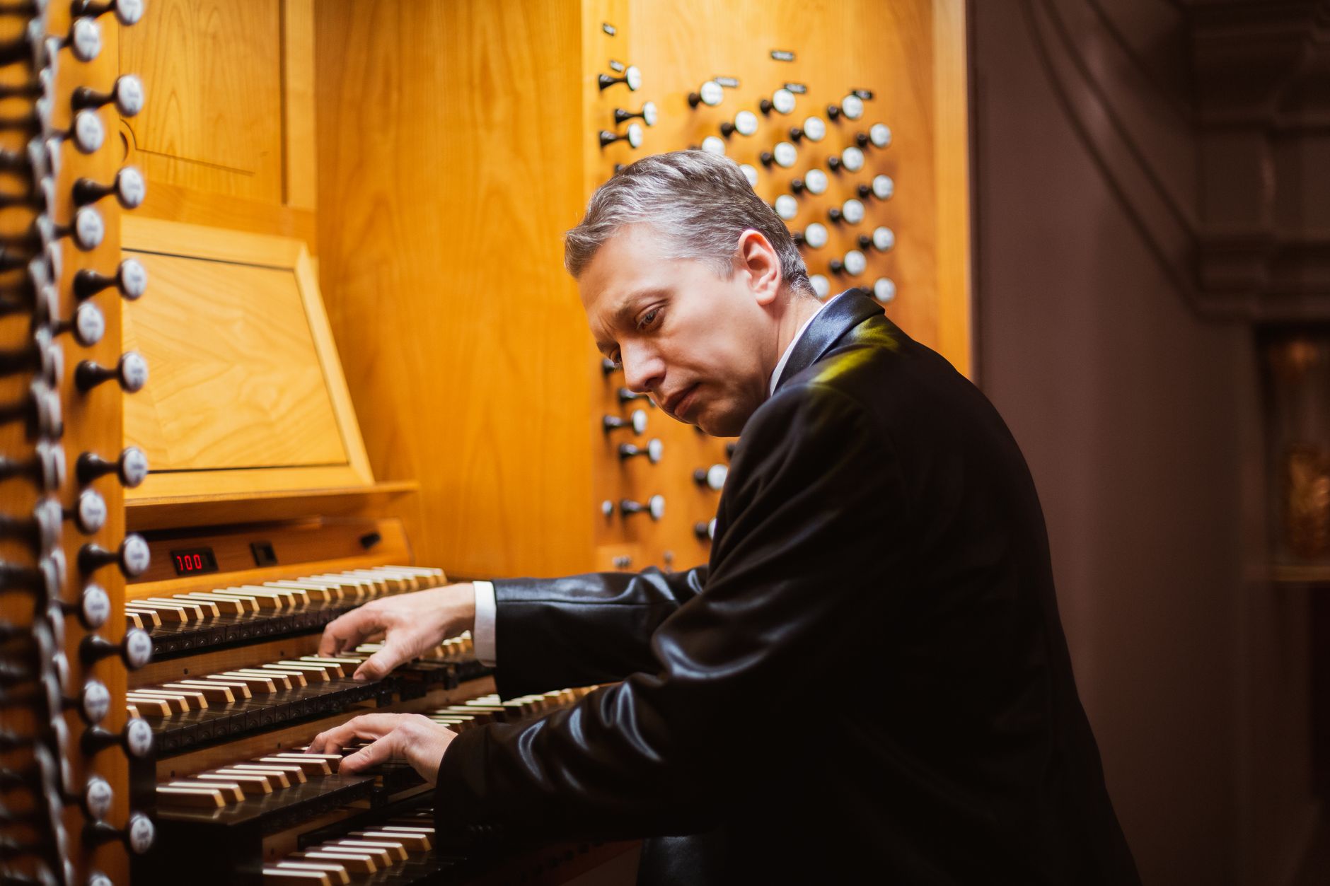 Elderly male organist performing on a classic pipe organ indoors.