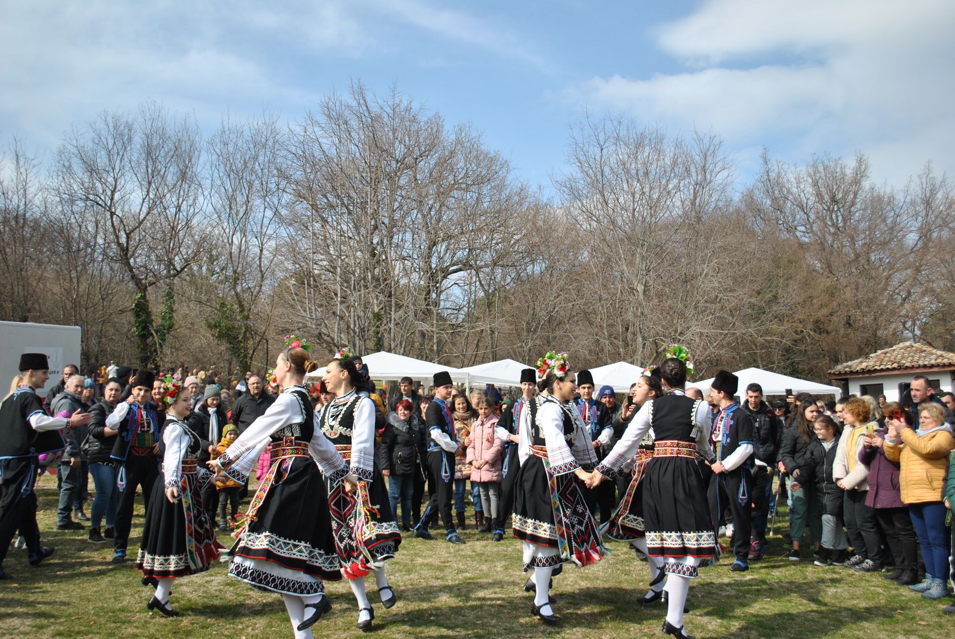 Outdoor festival scene featuring dancers in traditional attire performing cultural dance in front of a crowd.