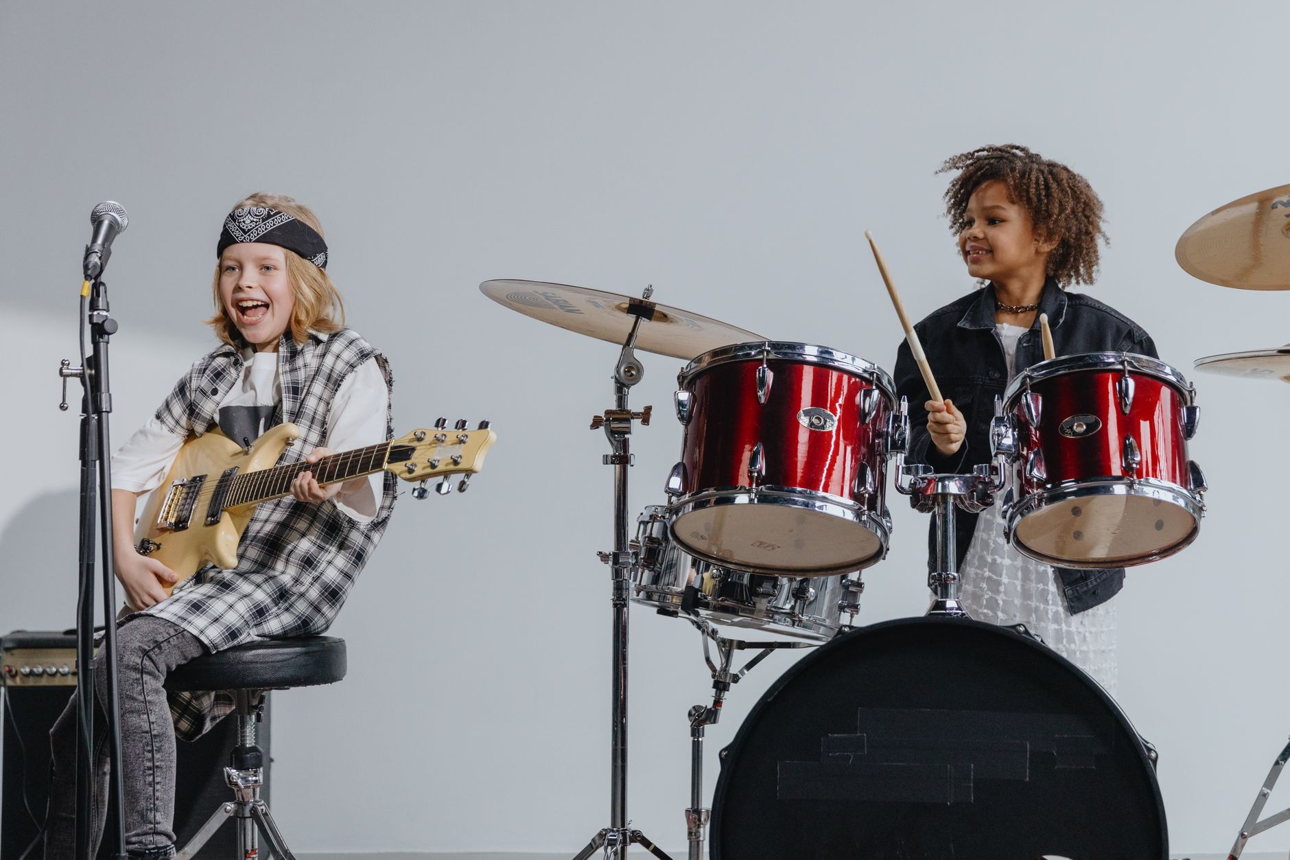 Children in a rock band play guitar and drums, creating music together on stage.