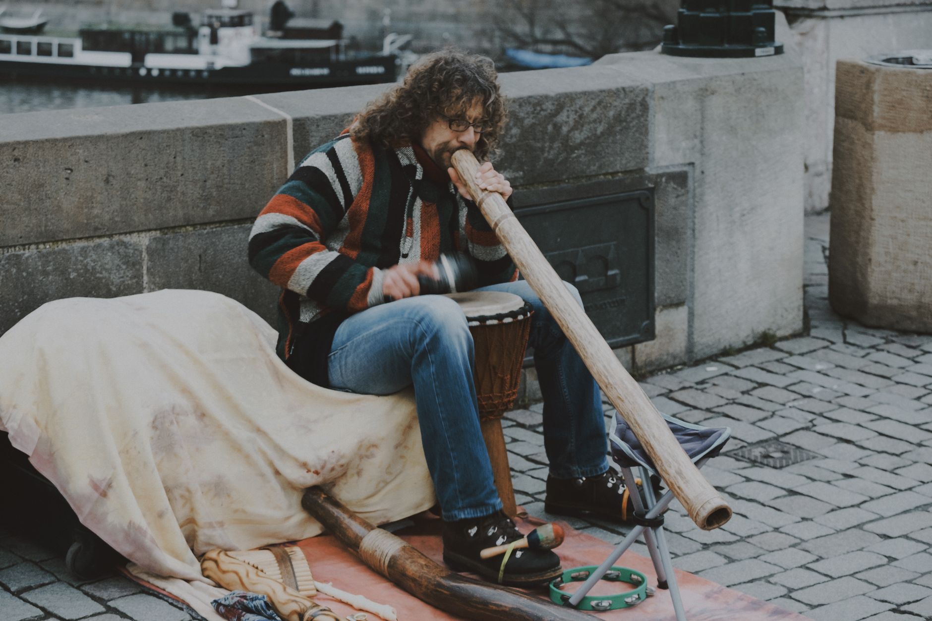A street musician performs with a didgeridoo and drum in an urban setting.