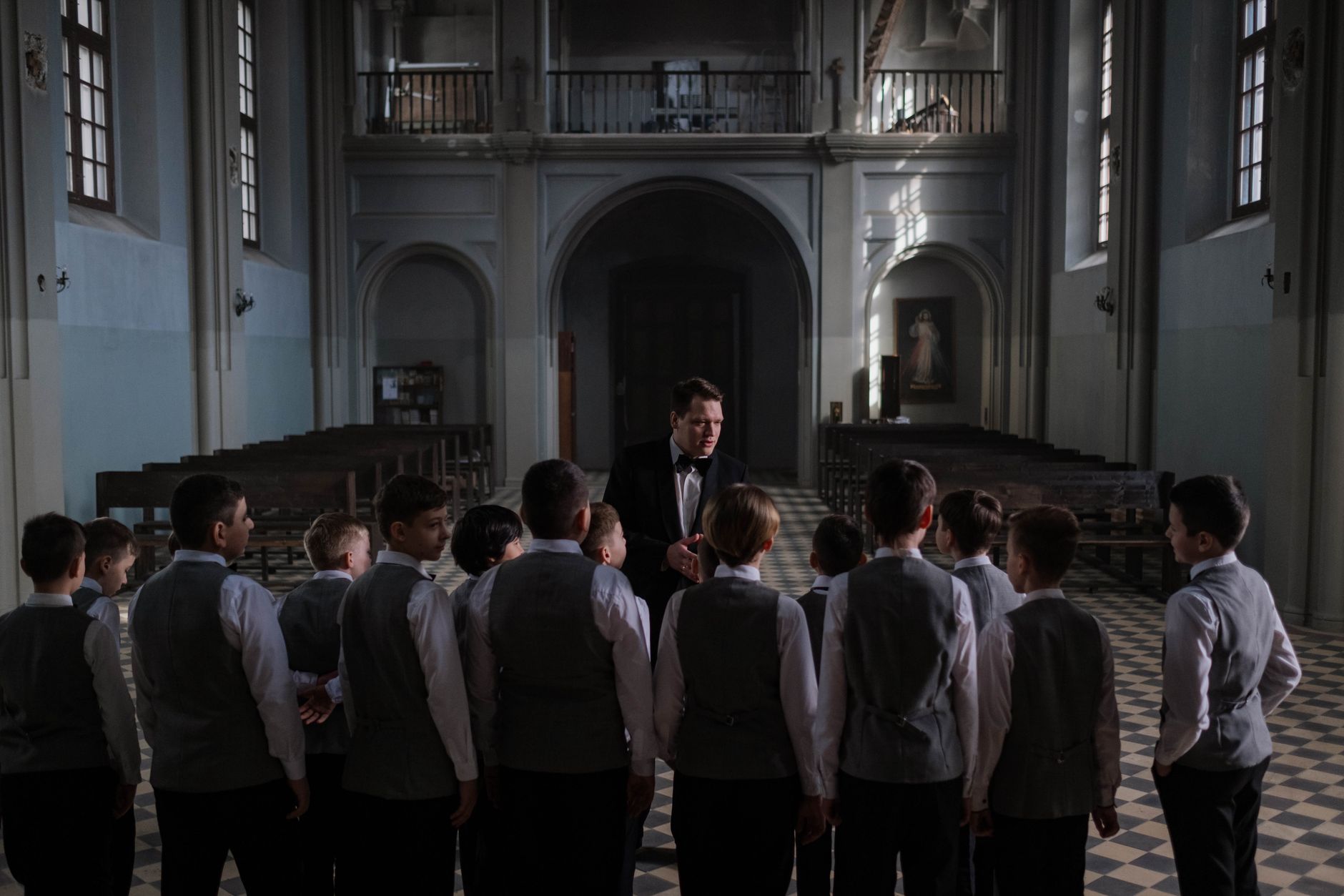 Boys choir rehearsing under conductor in an elegant cathedral setting.