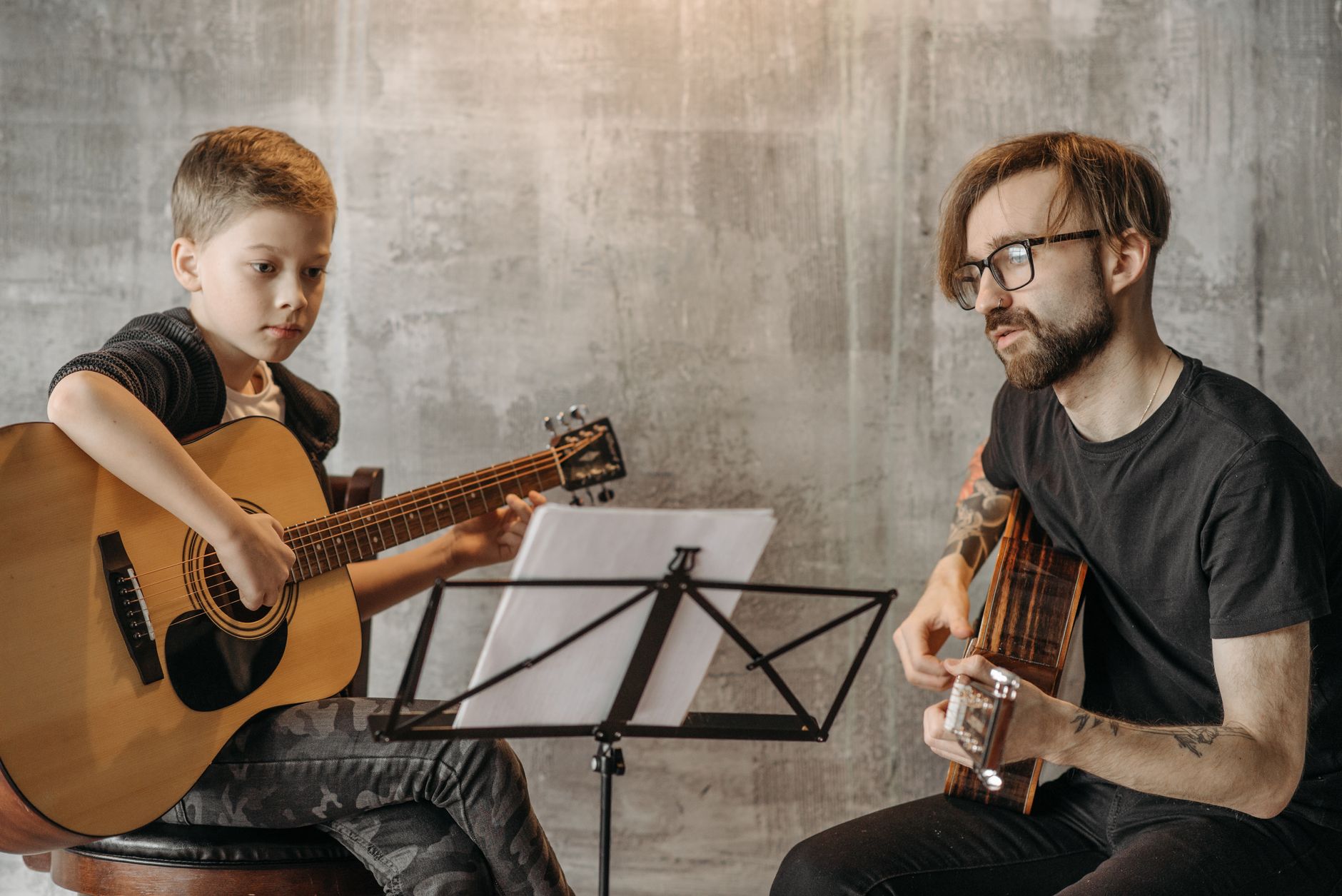 A young boy learns guitar from a teacher during a lesson indoors.