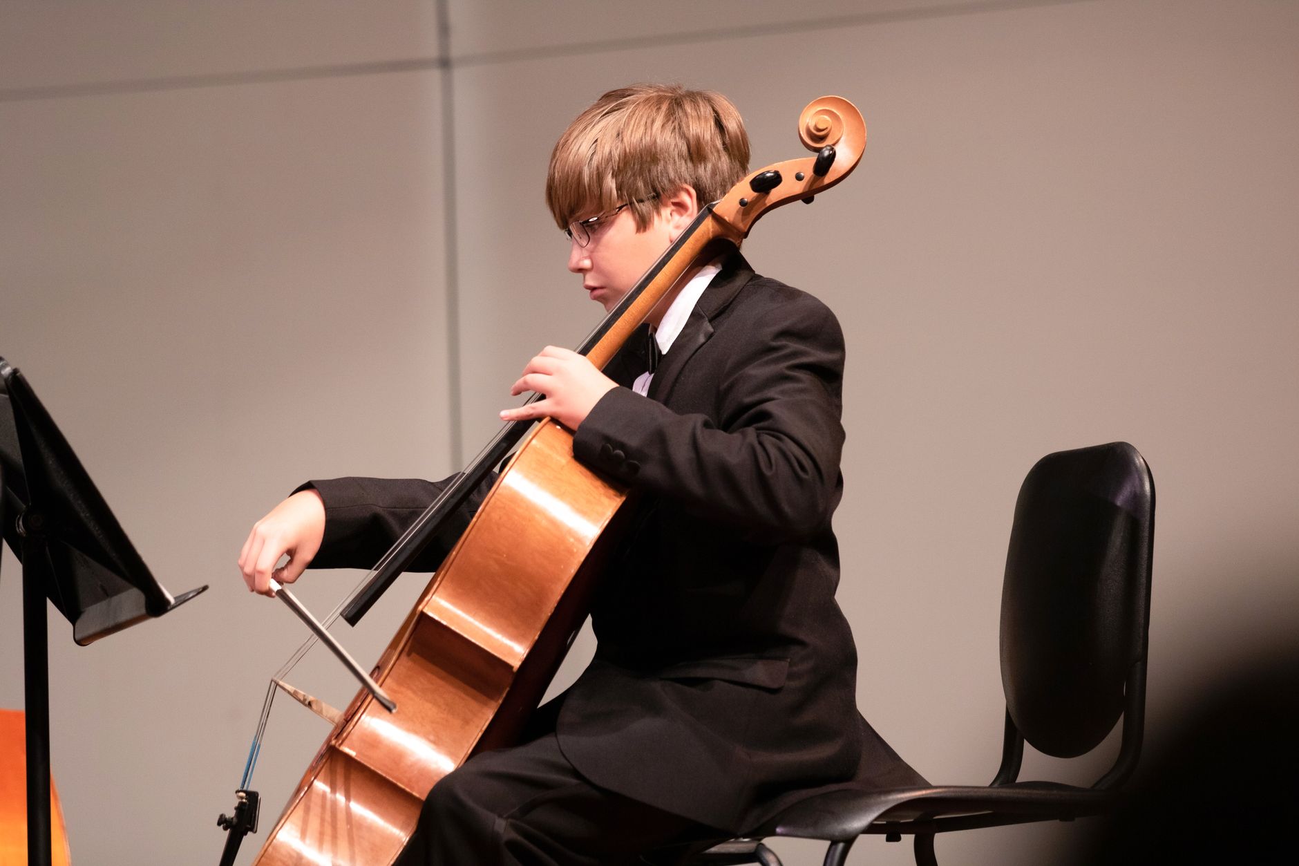 A young boy in a suit plays the cello during an indoor classical music performance.