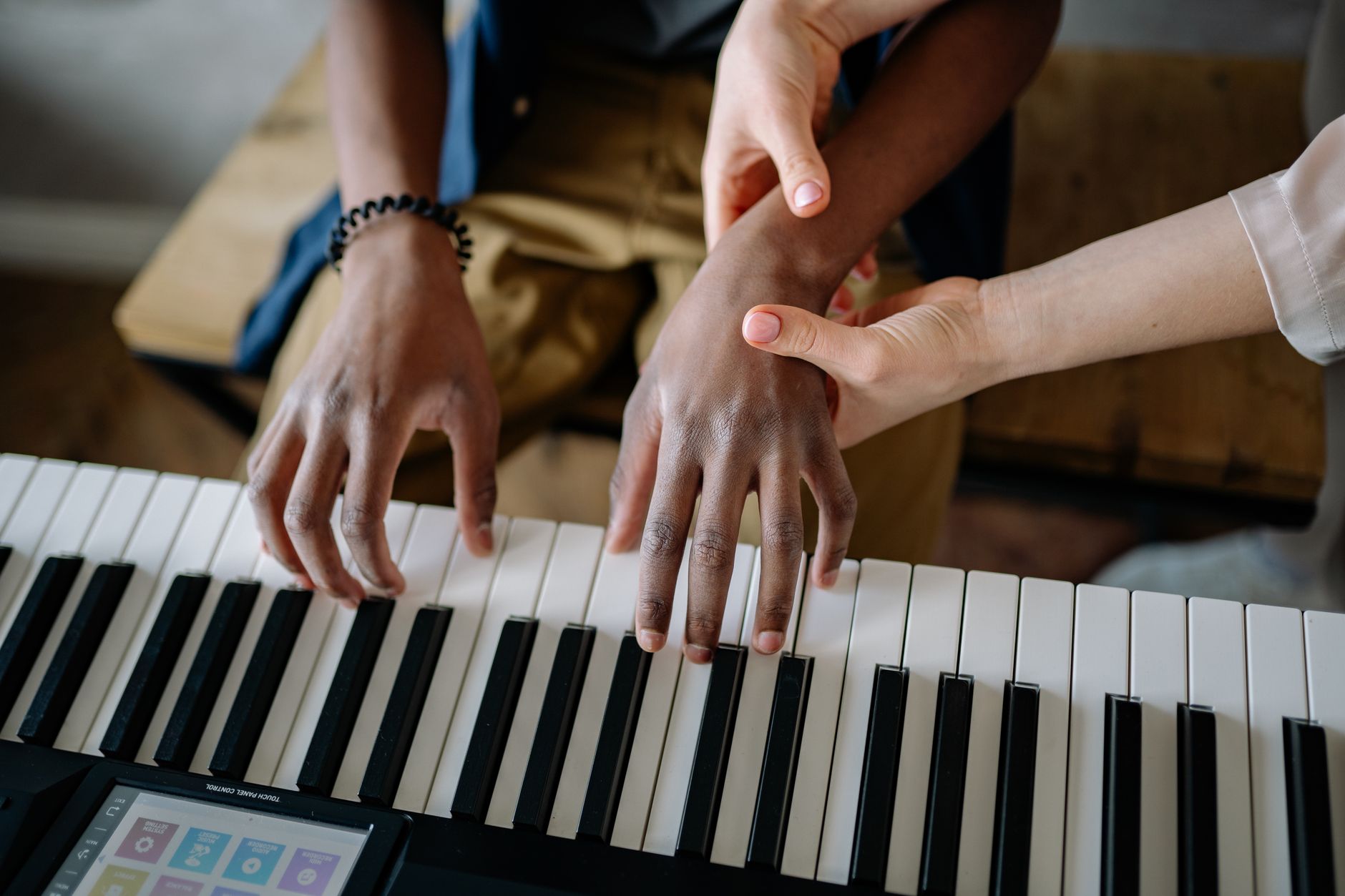 A music teacher guides a student on piano keys, emphasizing hands-on learning.