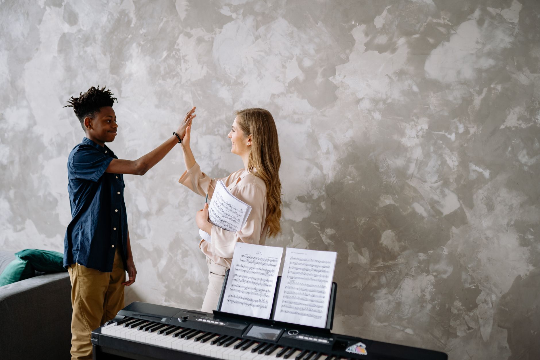 A student and teacher share a high-five during a piano lesson, showing enjoyment and connection.