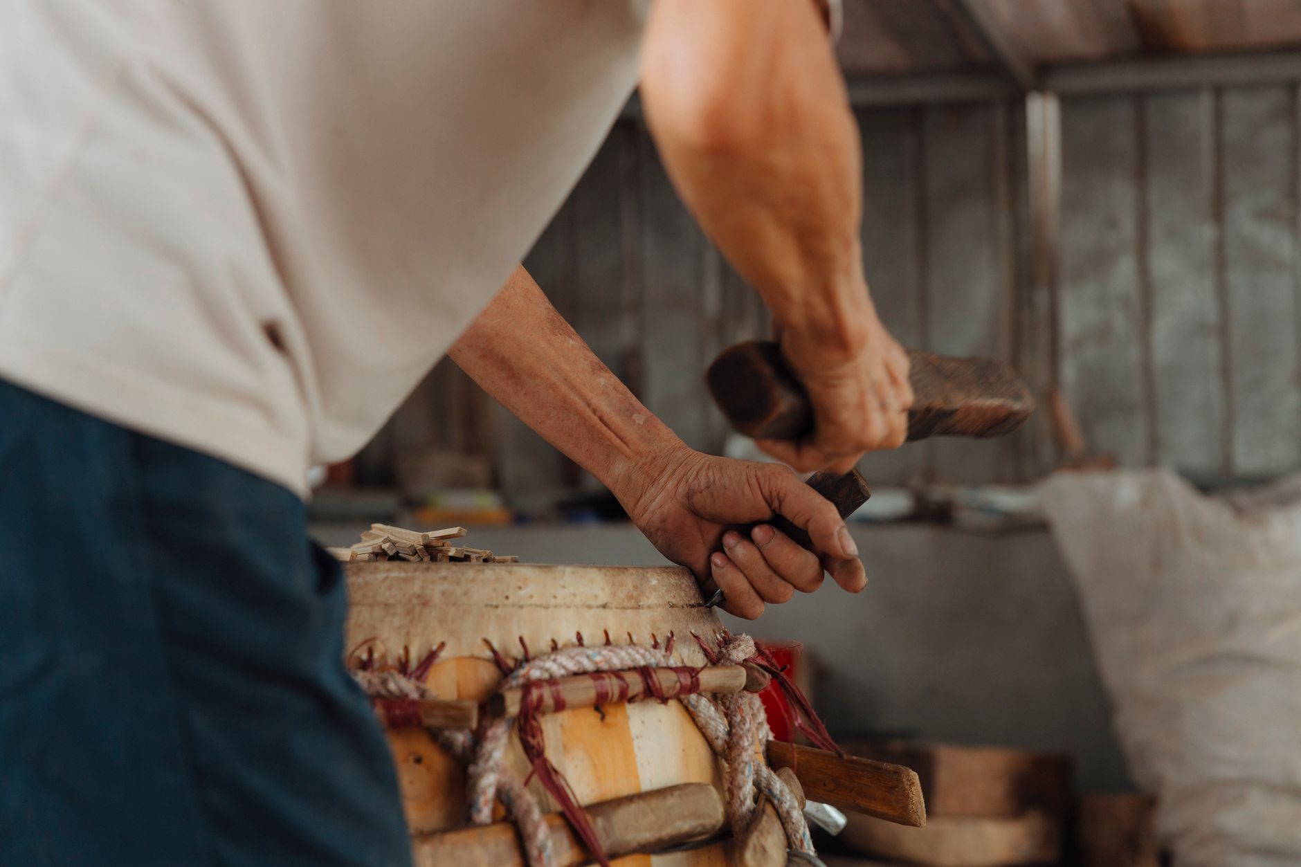 Close-up of a craftsman carving a drum in a workshop setting.