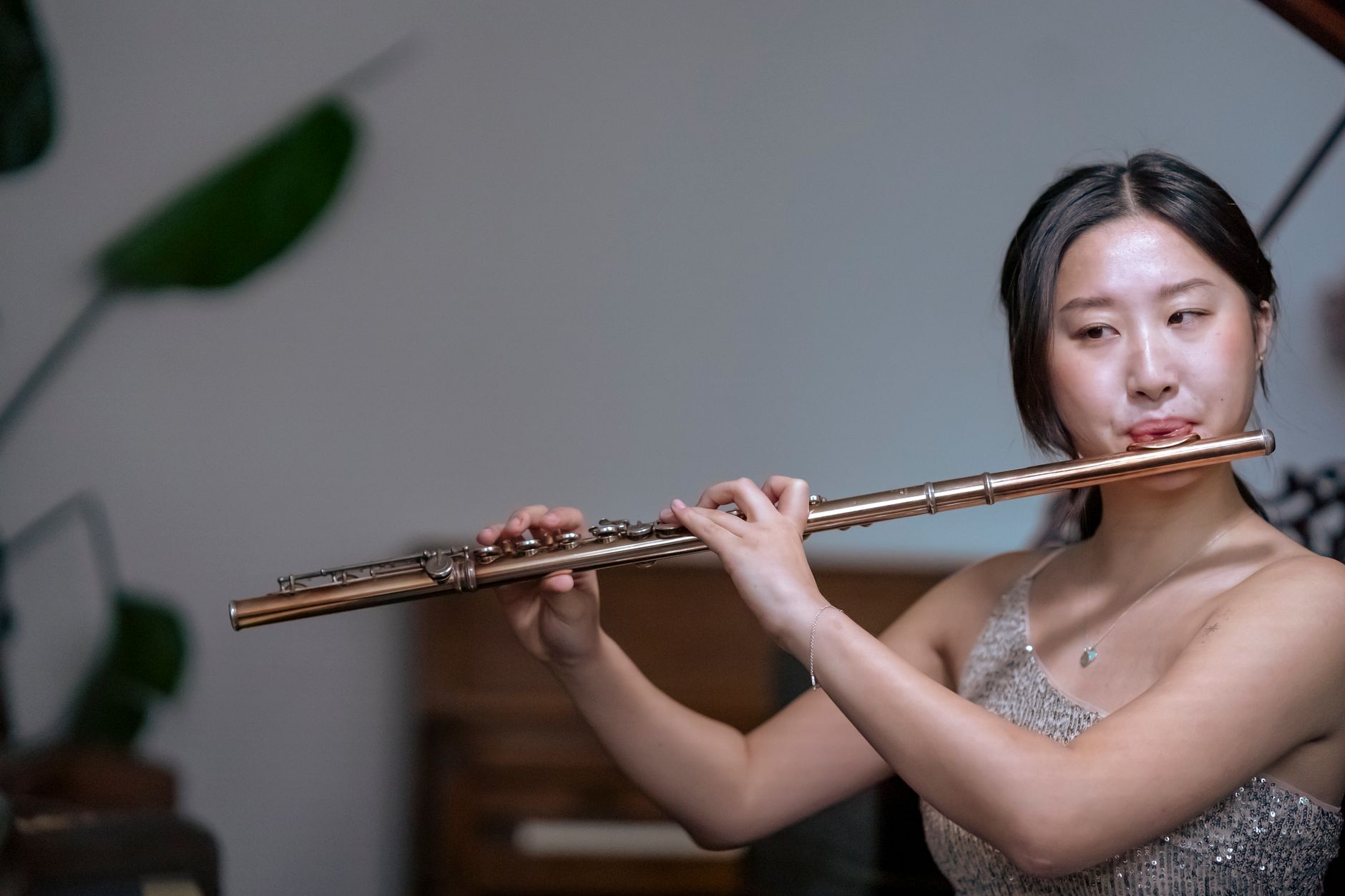 Talented ethnic female musician in shiny dress playing classic instrument flute while having live performance in concert hall