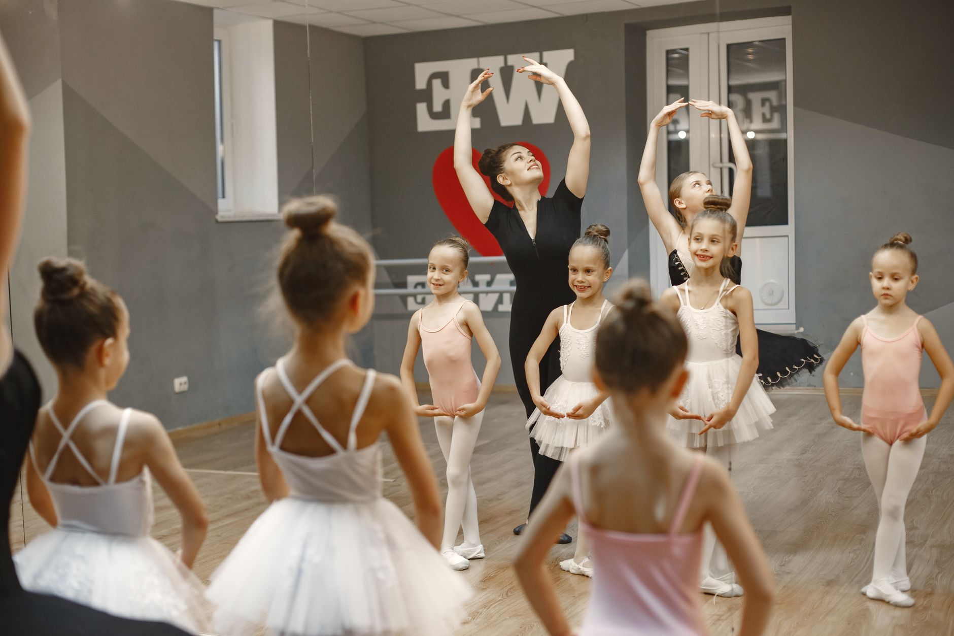 A group of young ballerinas practicing ballet poses under a teacher's guidance in a dance studio.