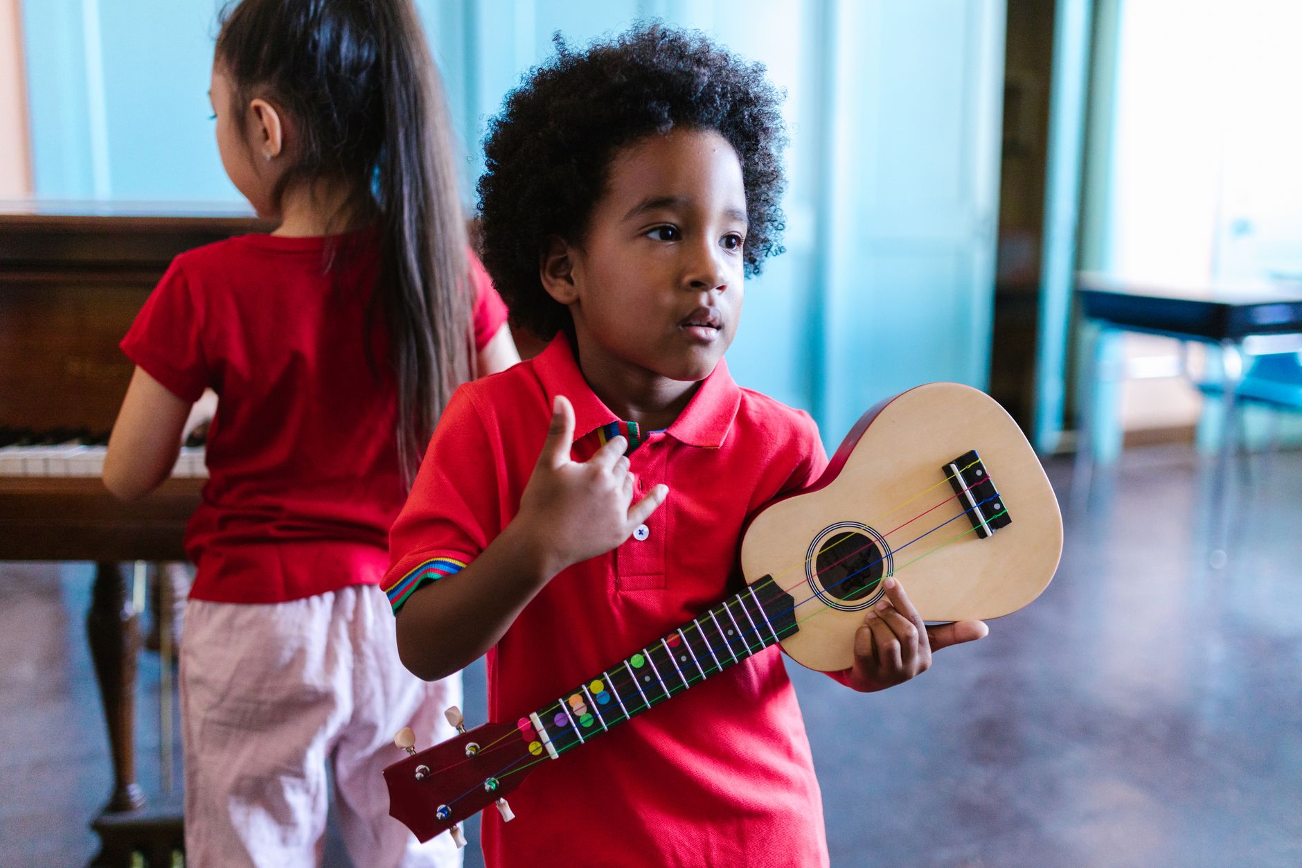 Two diverse children playing ukulele and piano in a bright room, showcasing musical learning.
