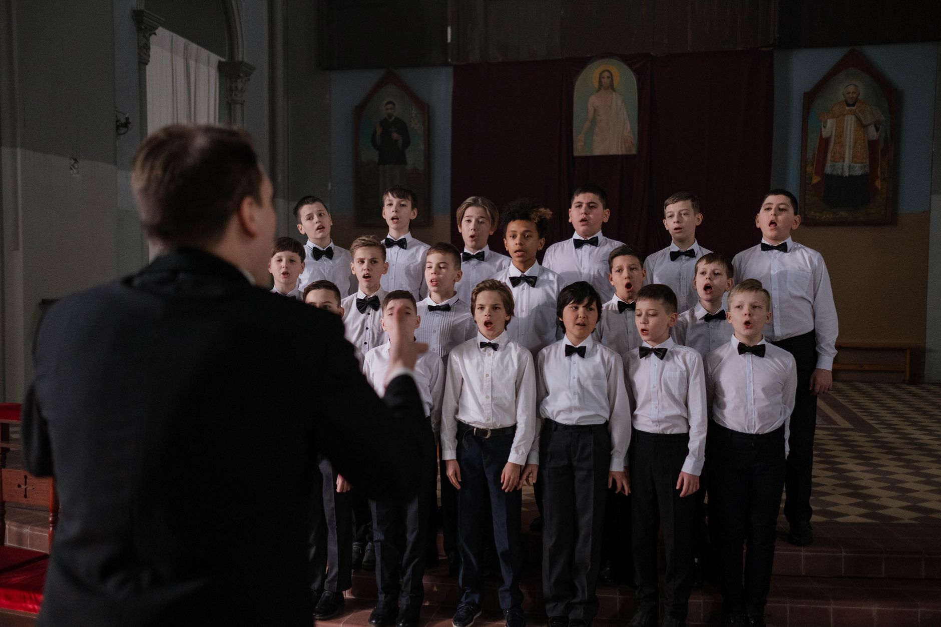 Boys choir in uniform singing under conductor's guidance in a church setting.