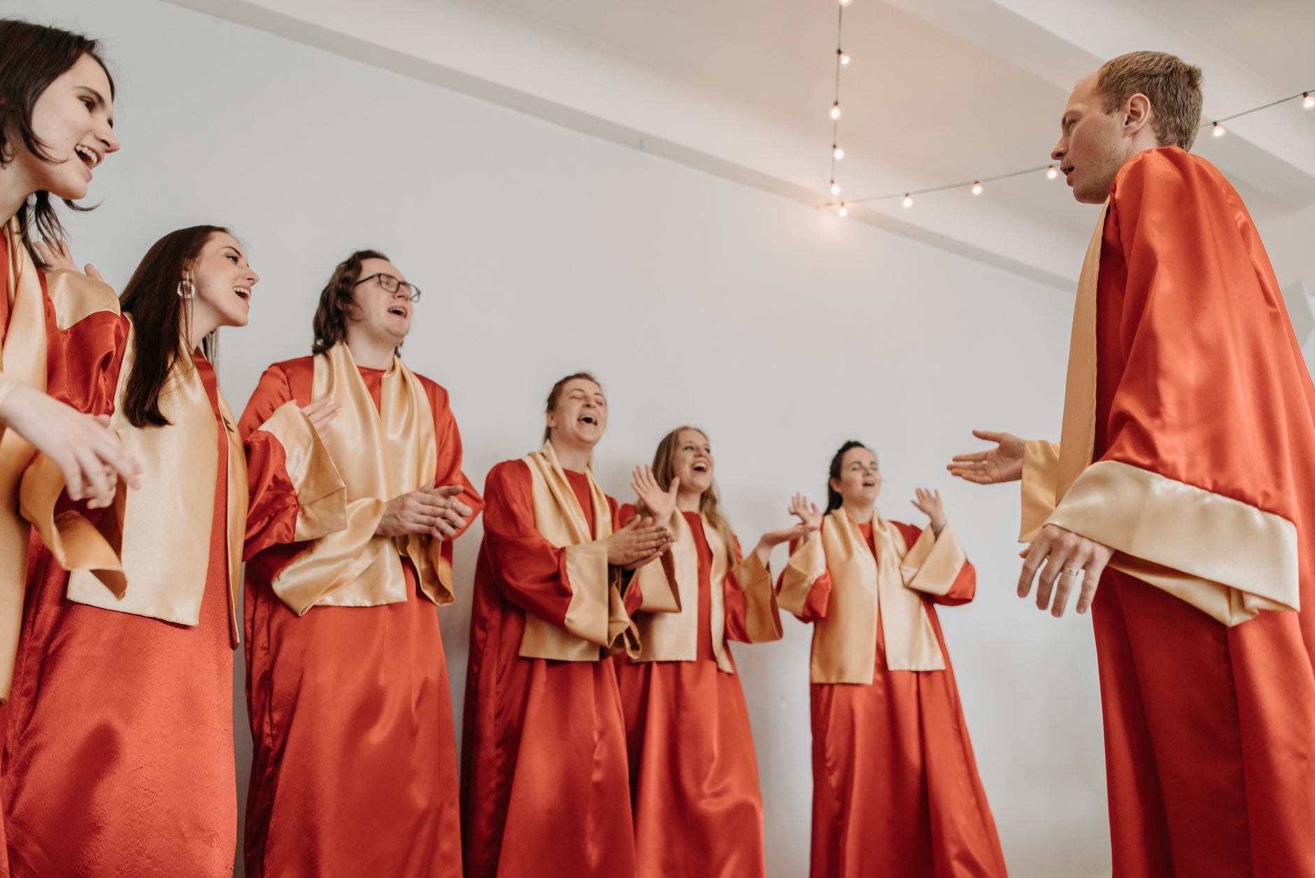 A diverse choir group joyfully sings in red and gold robes in an indoor setting.