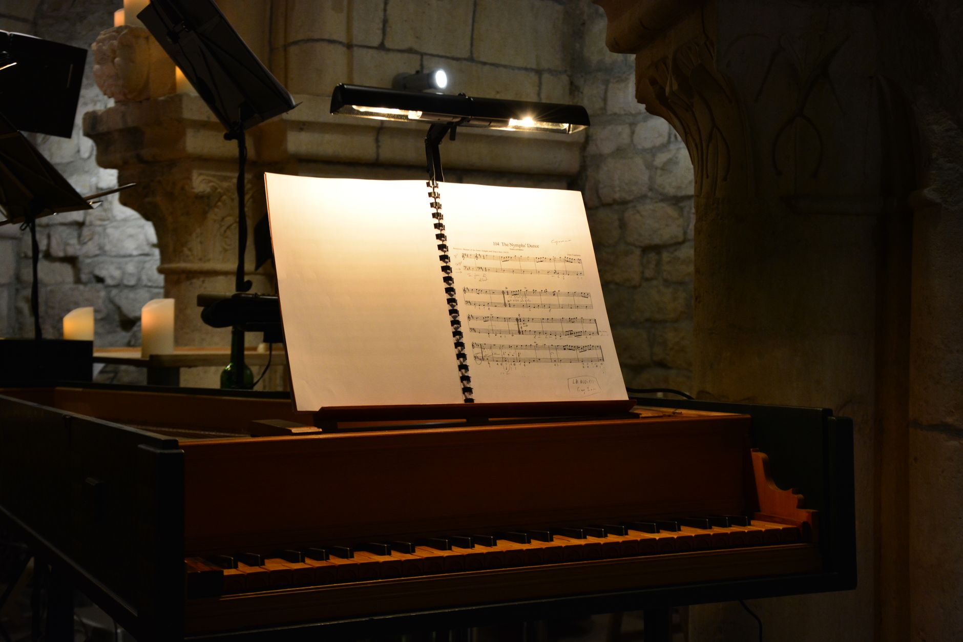 An evocative scene with sheet music lit on a harpsichord in a dimly lit stone interior, evoking a classical music ambiance.