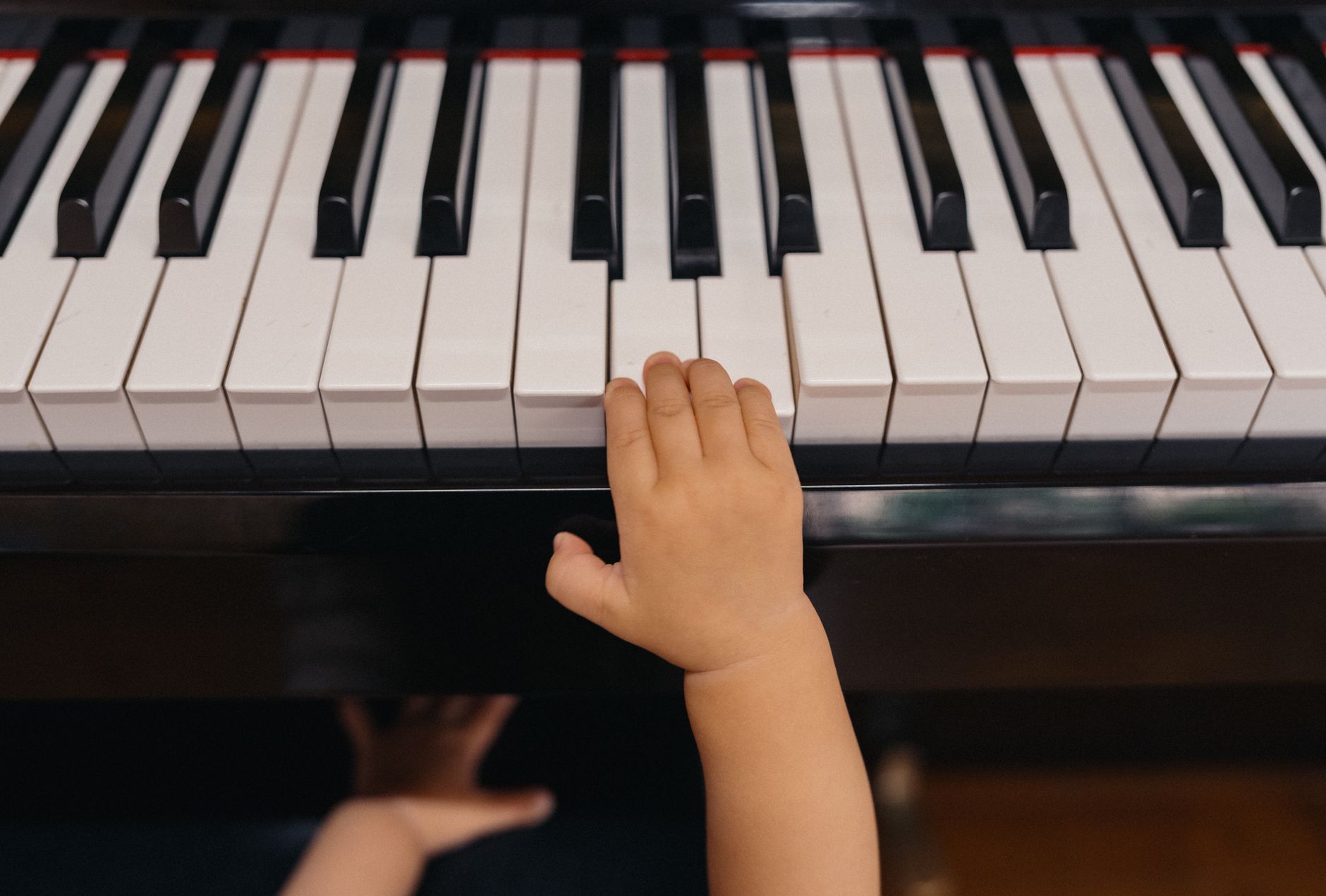 A close-up of a child's hand reaching for piano keys, showcasing early musical exploration.
