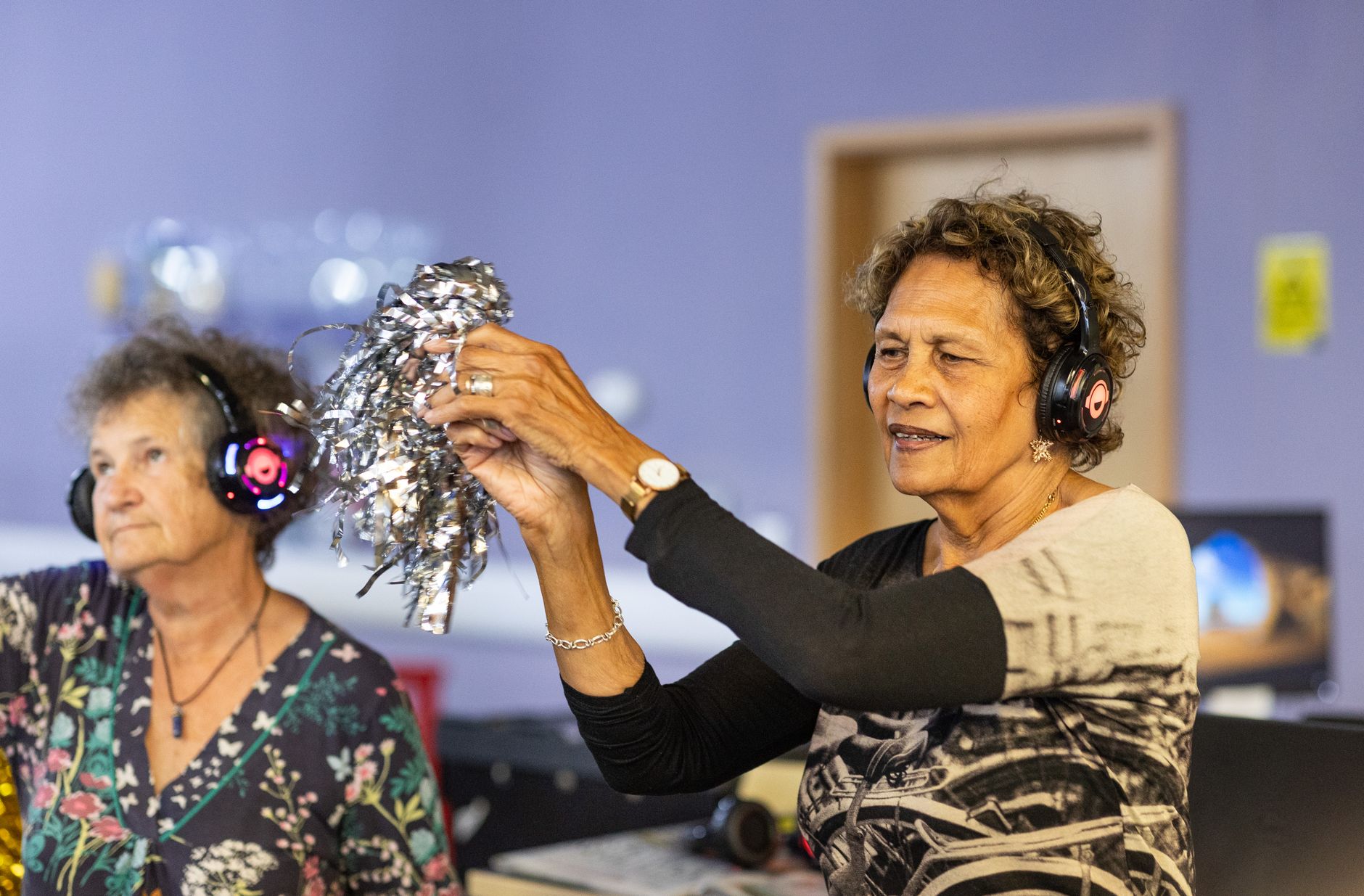 Elderly women with headphones dancing joyfully indoors, celebrating life with music.