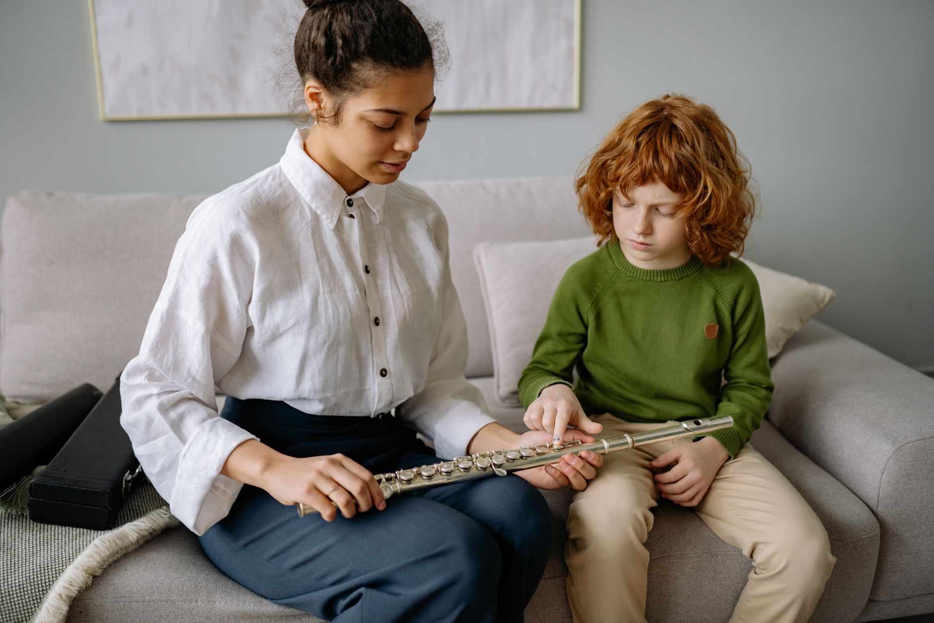 A music teacher guides a boy in playing the flute during an at-home lesson, fostering musical skills.