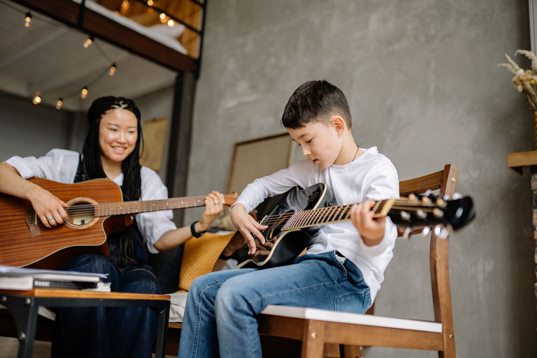A young boy learning guitar with a music teacher at home, focused and joyful.