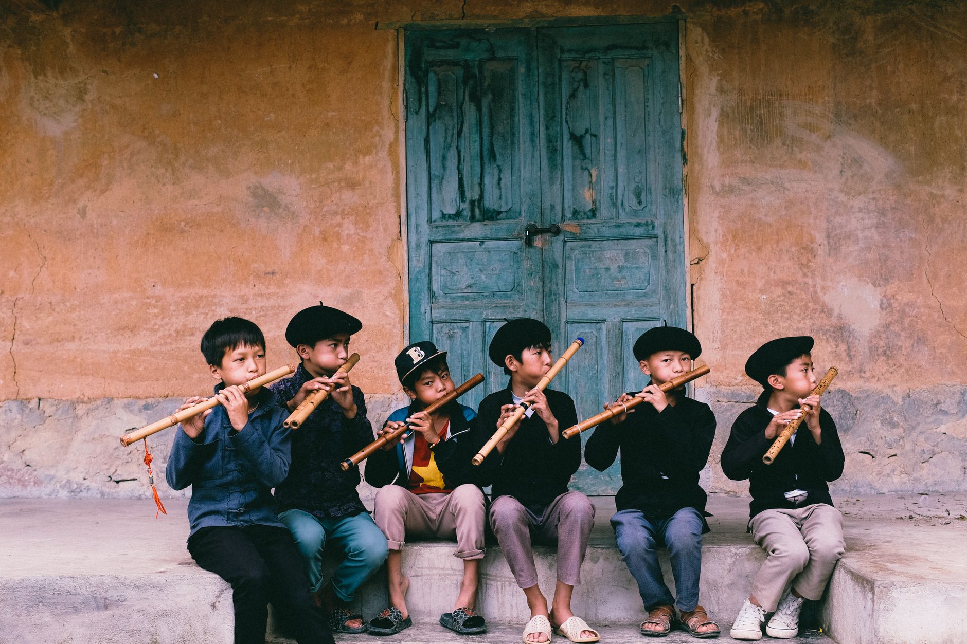 Group of boys playing traditional flutes in front of old door in Hà Giang, Vietnam.