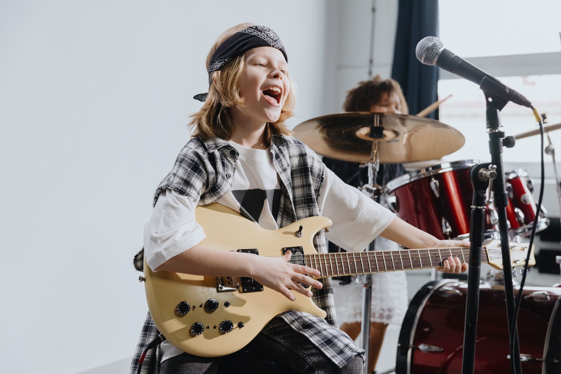 Energetic young girl playing electric guitar and singing into a microphone on stage.