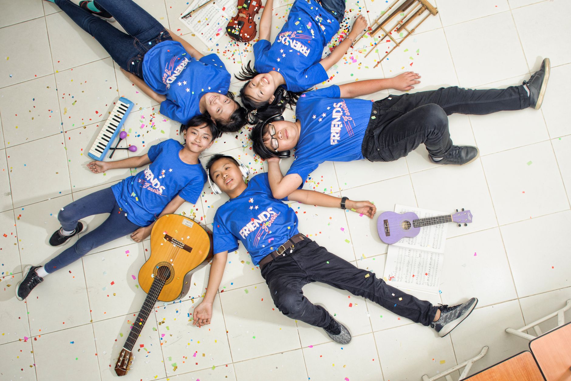 Children lying on a tiled floor with musical instruments and confetti, enjoying a creative moment.