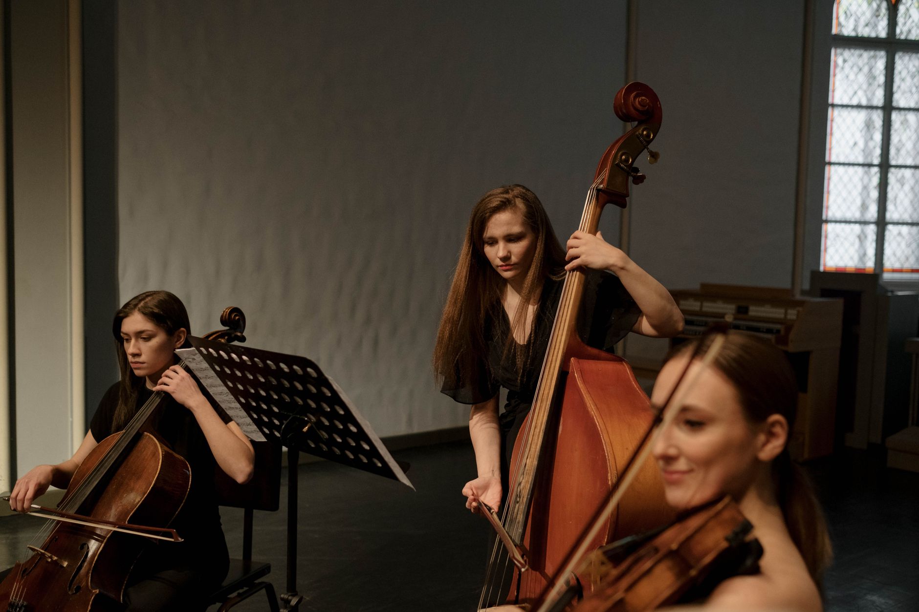 A trio of female musicians playing string instruments in a chamber music setting.
