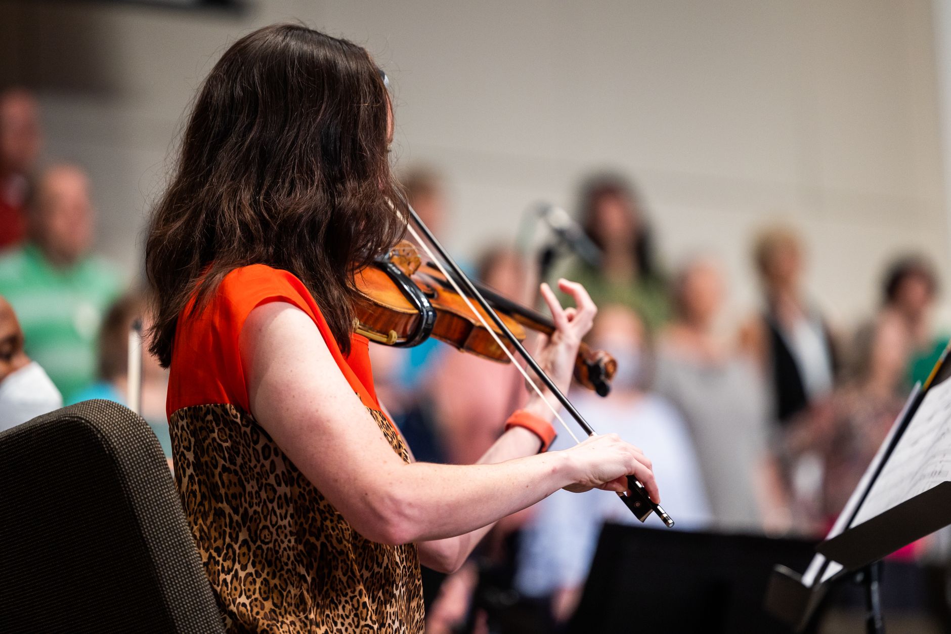 A violinist passionately playing during an indoor concert with an audience in the background.
